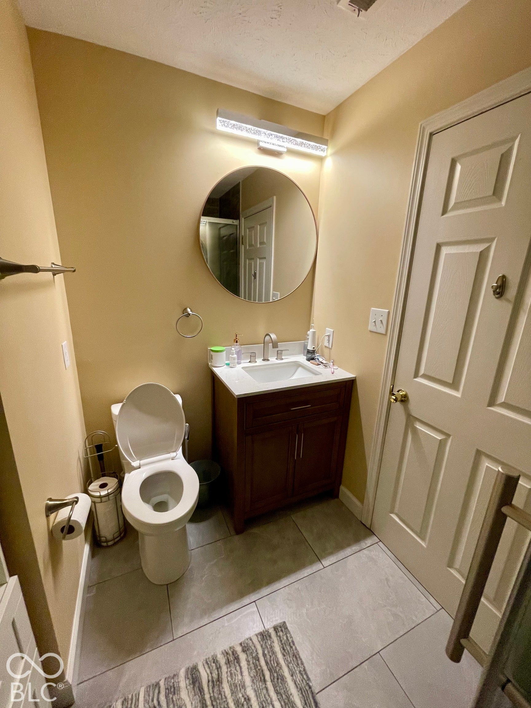 Floor-mounted toilet, vanity with integrated sink, chrome faucet, modern circular mirror, and overhead linear vanity lighting...Hall Bath