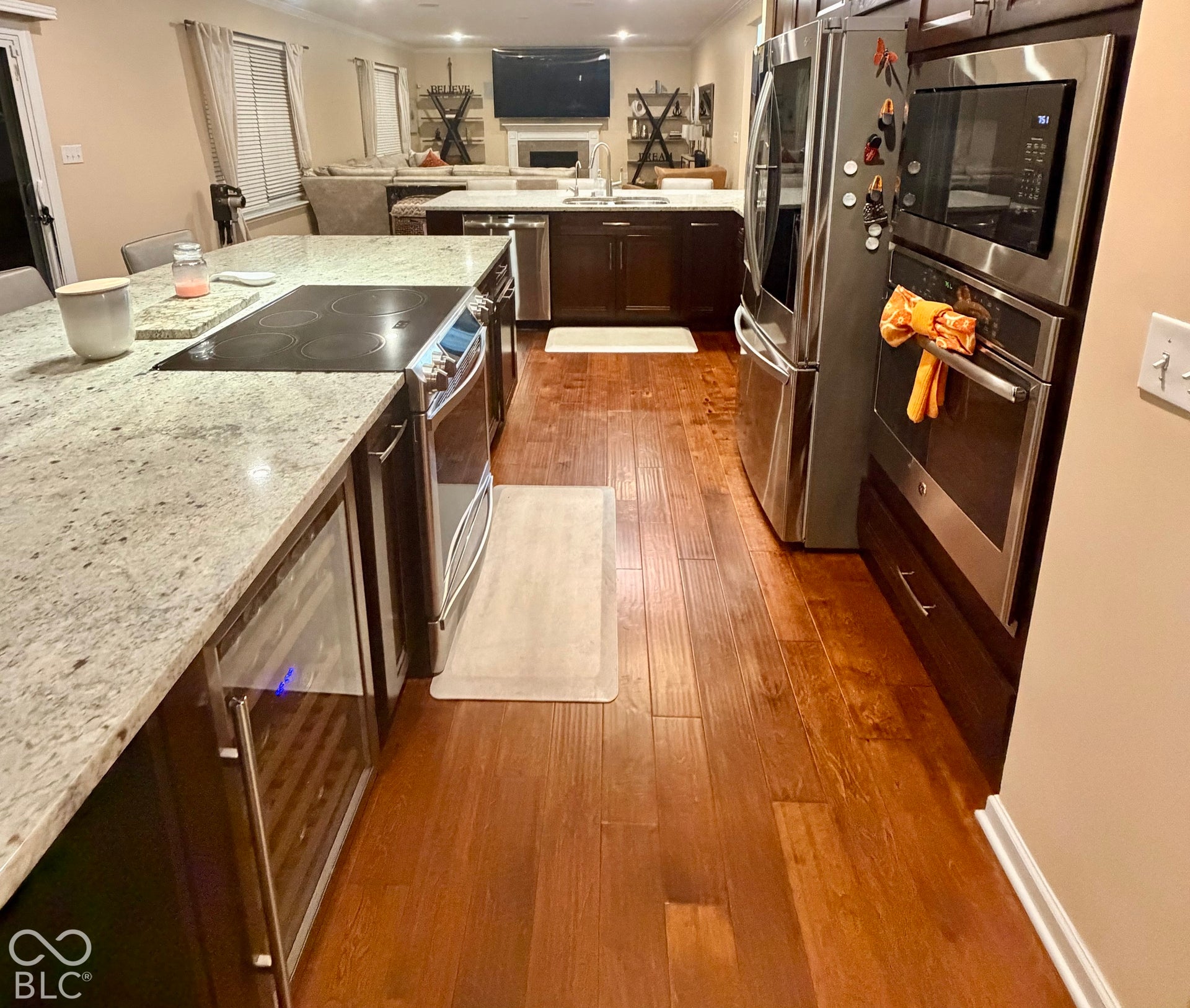 Kitchen featuring wood-finish flooring, stainless steel appliances, granite countertops, an integrated cooktop, and a built-in beverage refrigerator
