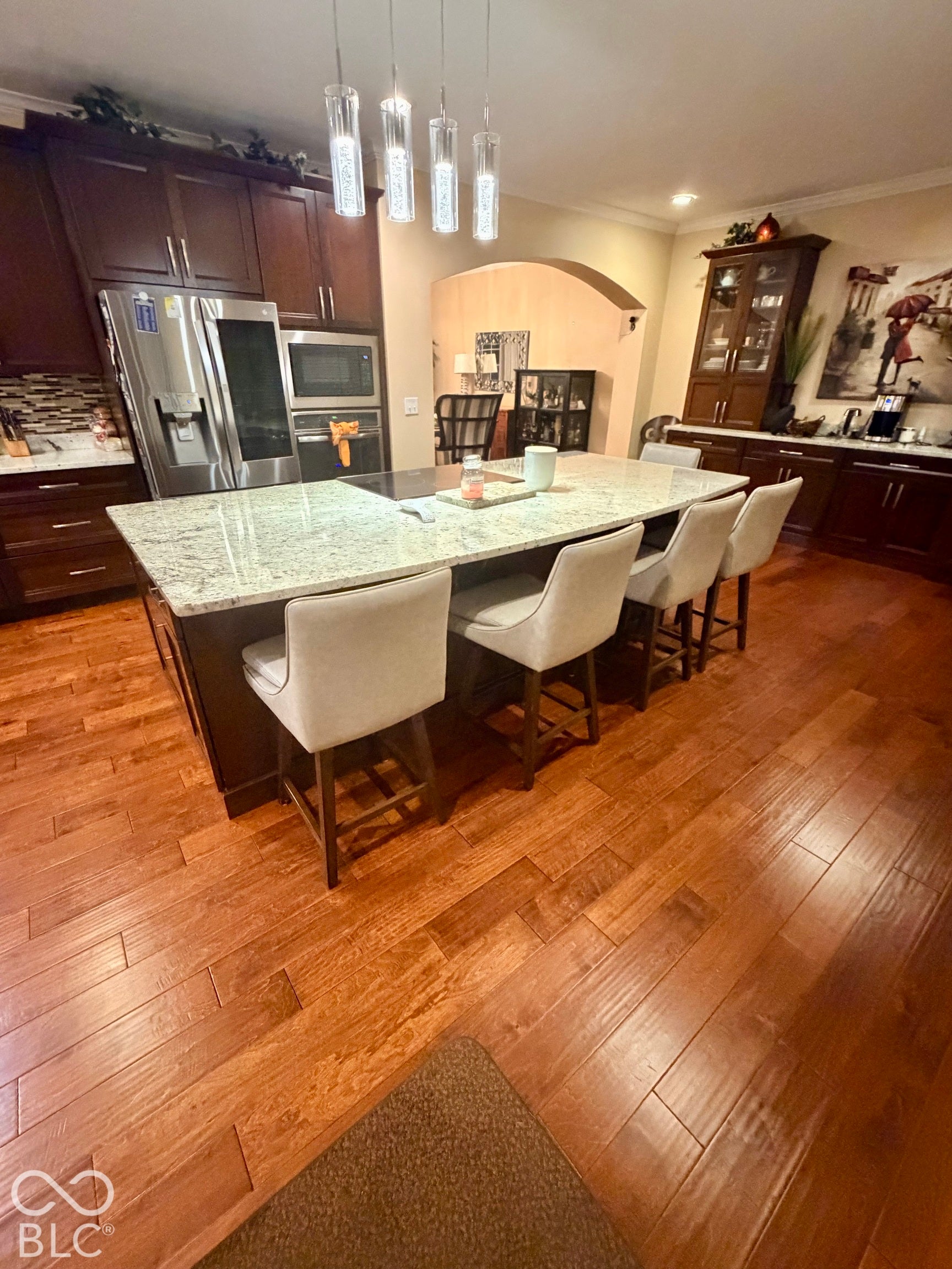 Kitchen featuring a large island with a light-toned countertop, stainless steel appliances, dark wood-finish cabinetry, and wood-finish flooring