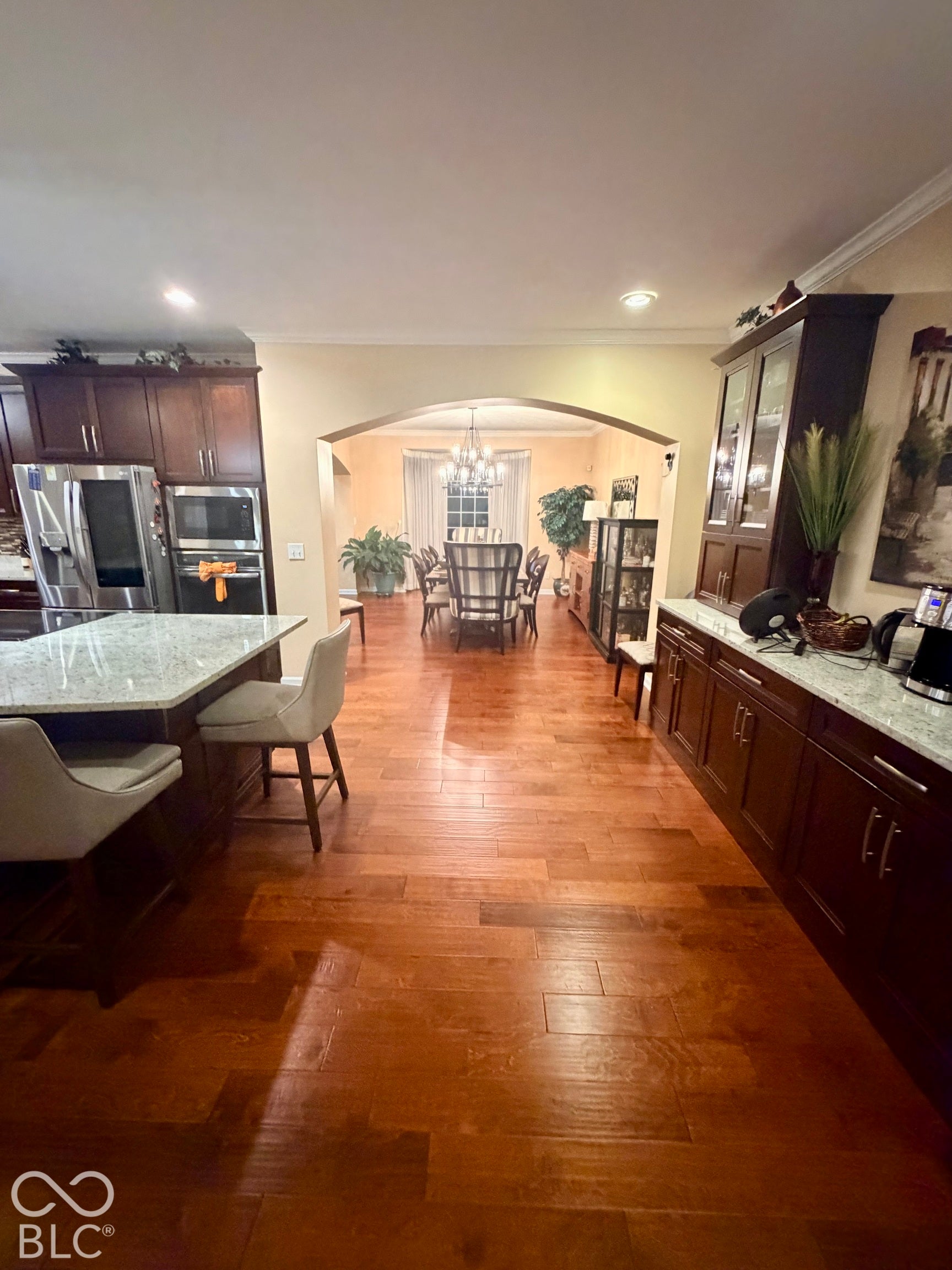 Wood-finish flooring throughout, dark wood cabinetry, granite countertops, stainless steel appliances, and an arched entryway