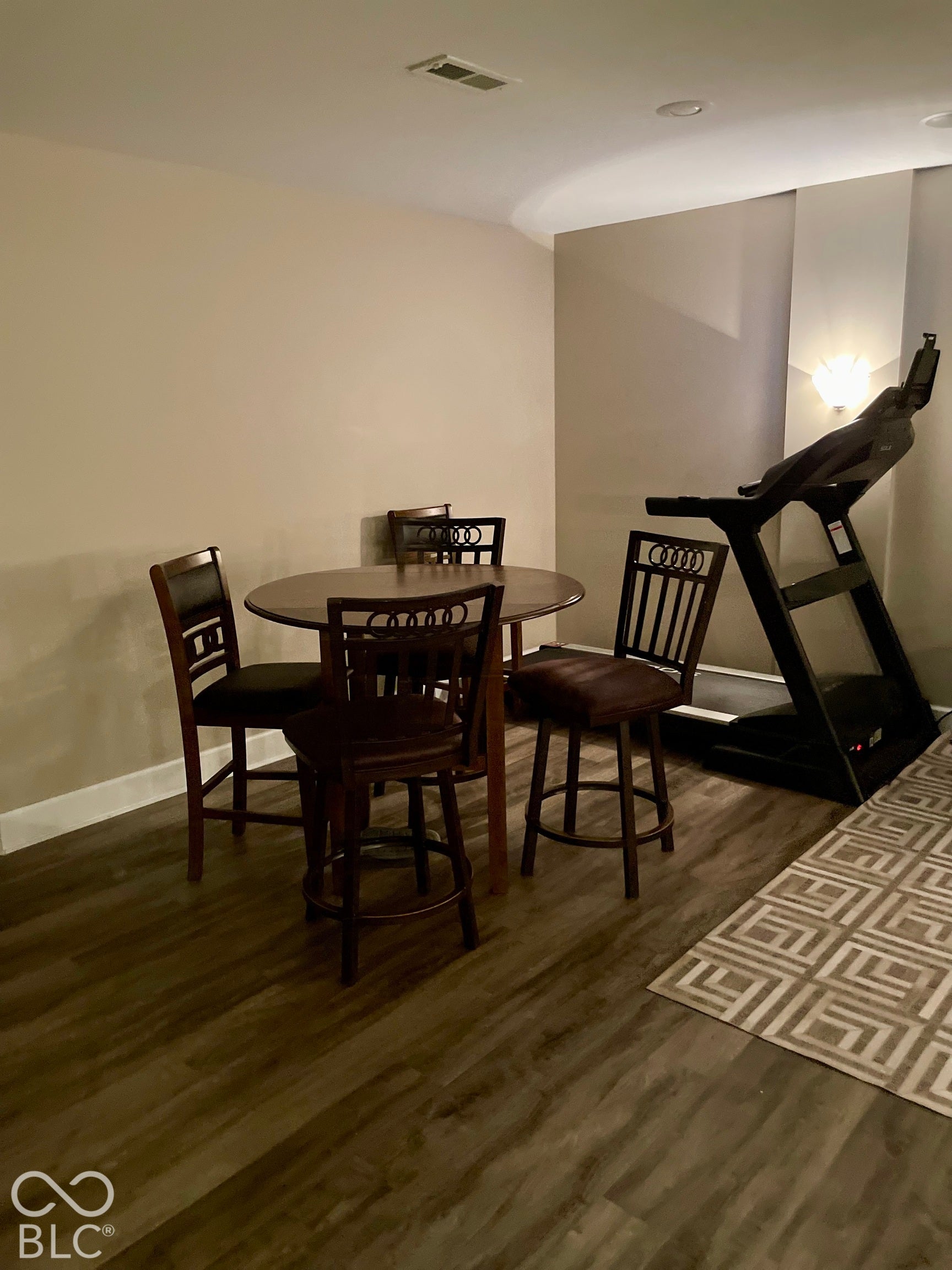 Wood-finish flooring with white trim, recessed ceiling lighting, and a wall-mounted sconce