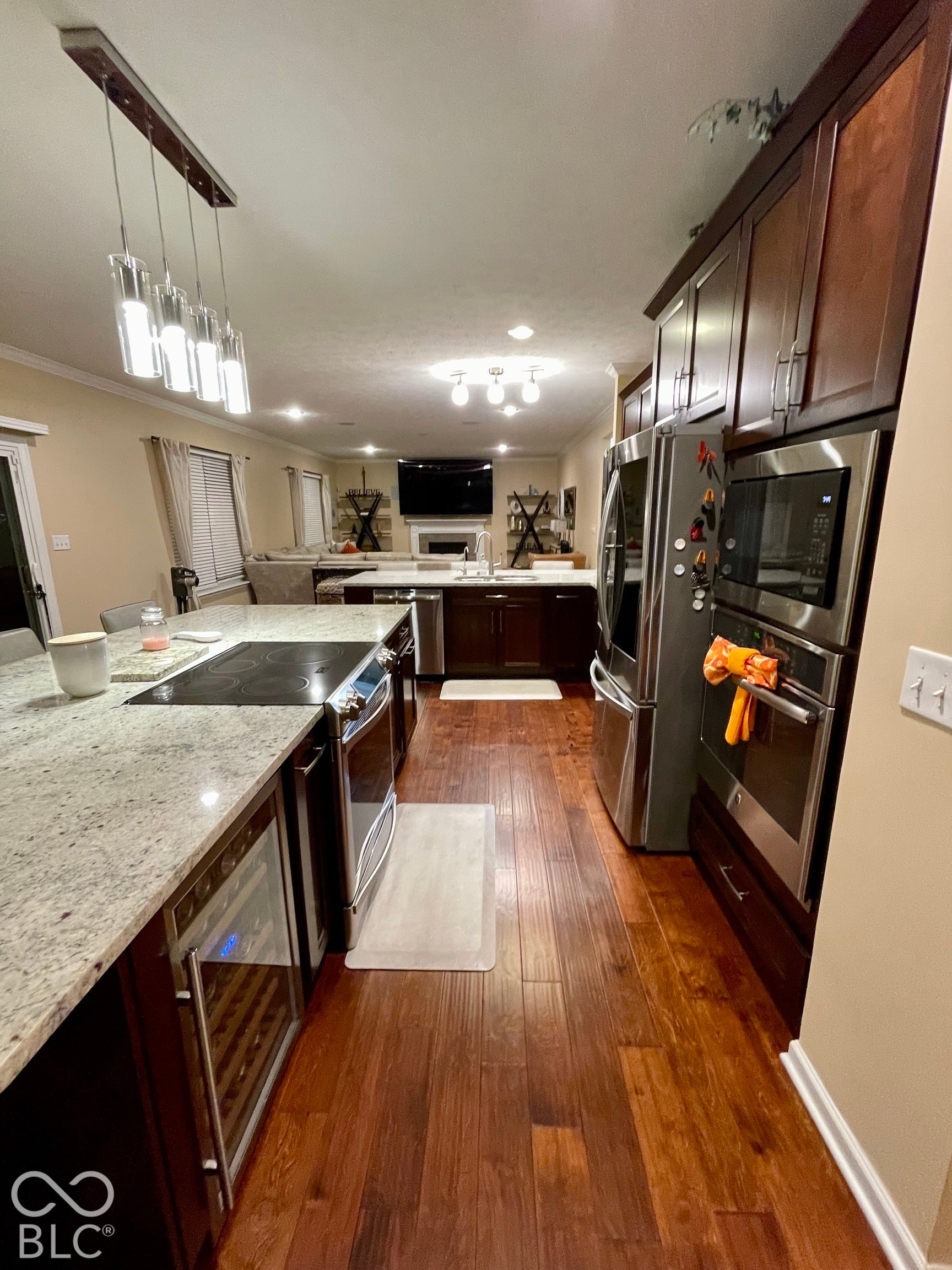 Kitchen featuring extensive wood-finish flooring, granite countertops, built-in stainless steel appliances, dark wood cabinetry, and recessed lighting