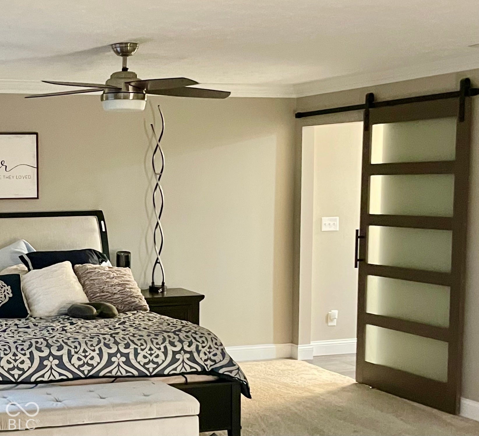 Barn door entry with frosted glass panels, crown molding, ceiling fan with light fixture, and plush carpet flooring
