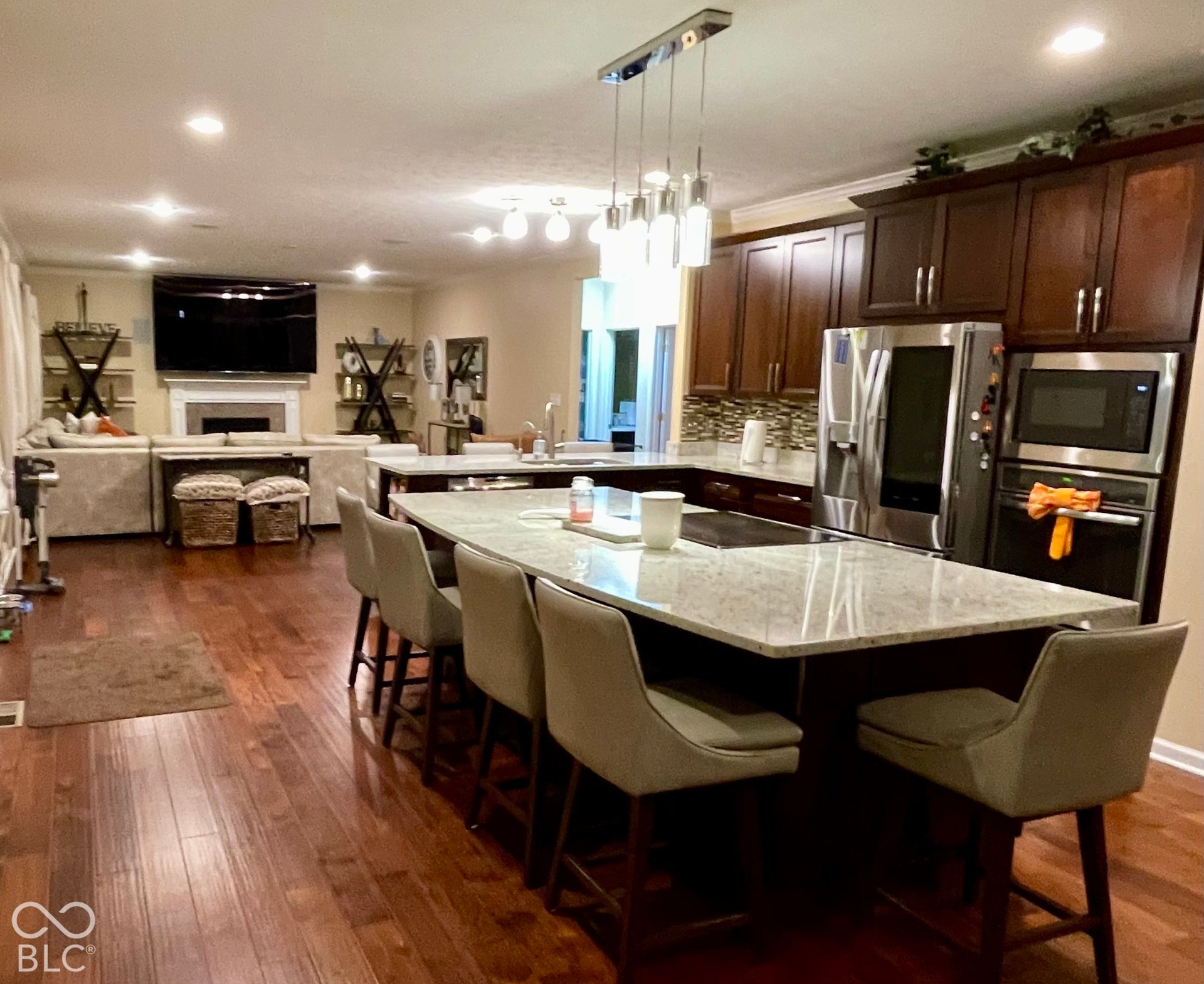 Expansive kitchen island with a light-toned countertop, rich wood-finish flooring, dark wood cabinetry, and stainless steel appliances