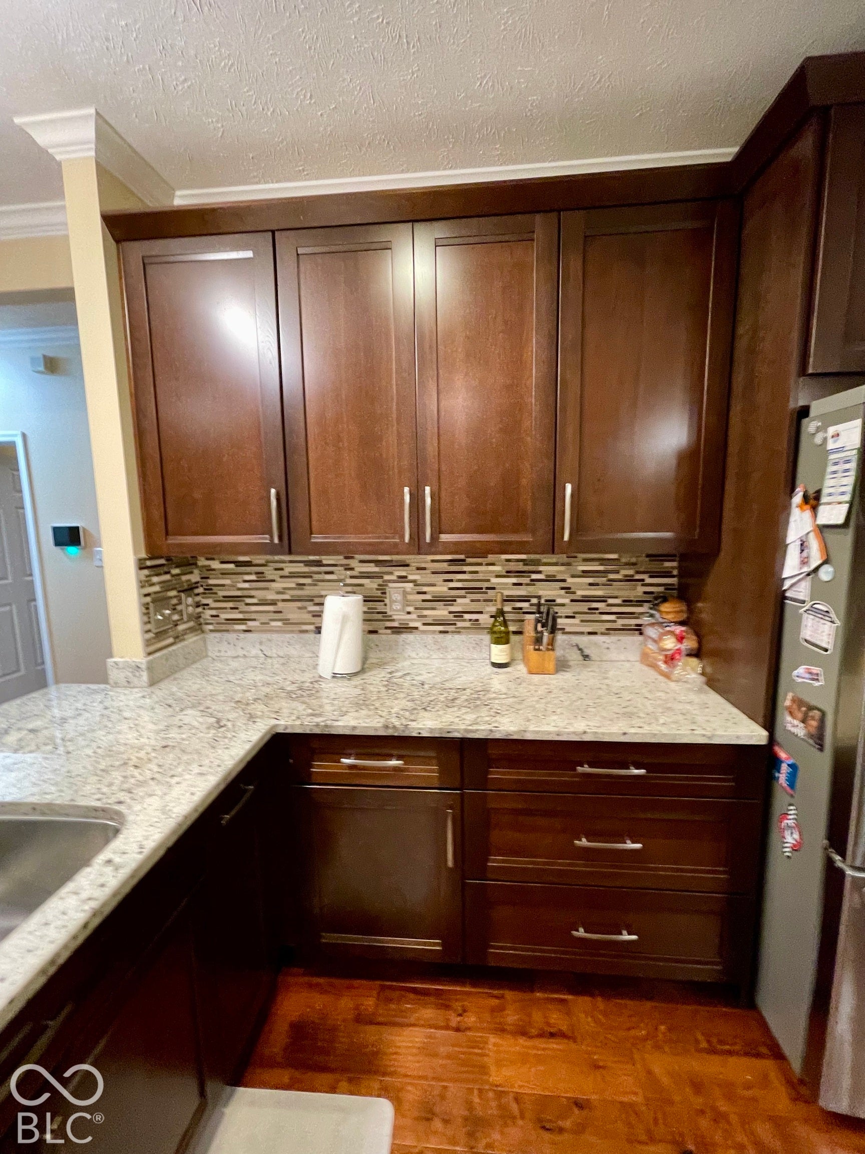 Granite countertops, a stainless steel sink, wood-finish flooring, dark wood cabinetry, and a mosaic tile backsplash