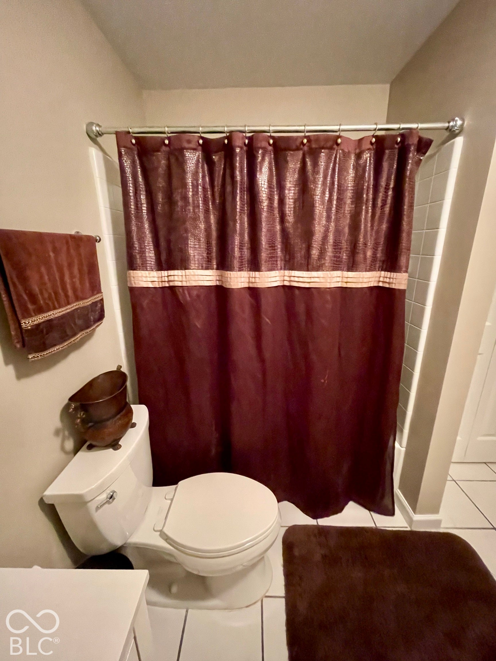 White ceramic toilet, white tiled flooring, and a white shower surround
