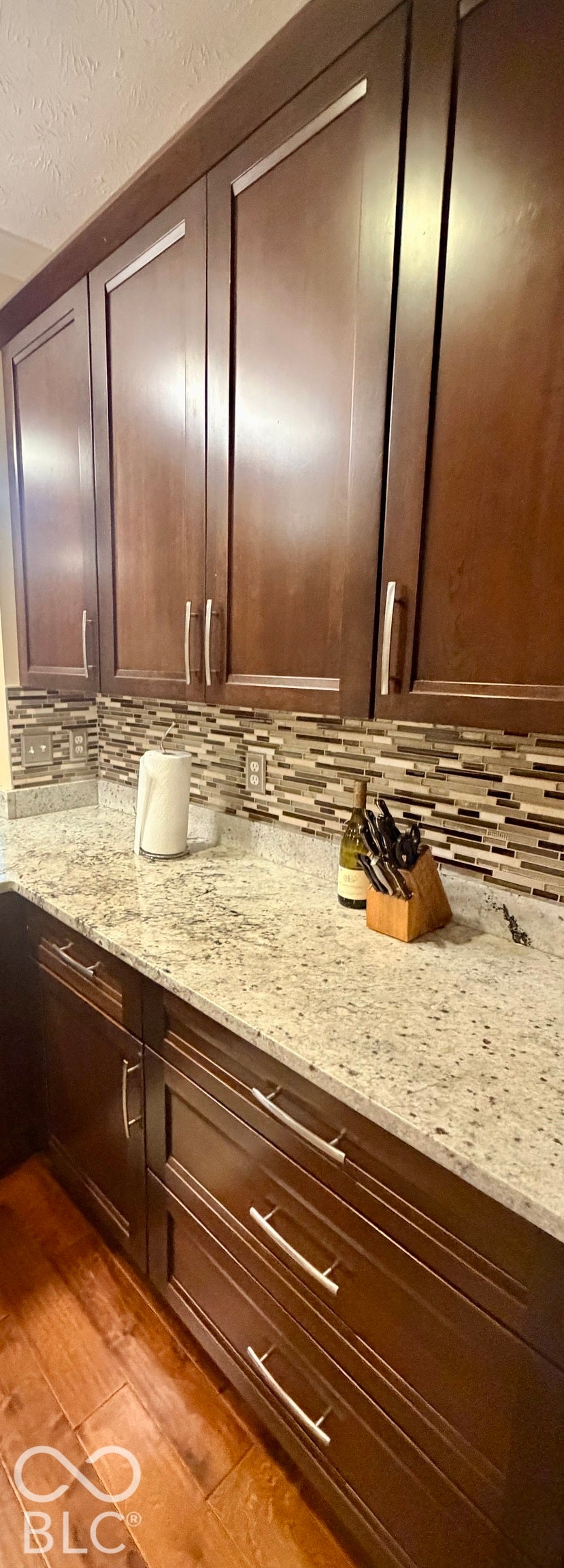 Rich wood-finish cabinetry, light-toned countertops, mixed material backsplash, and wood-finish flooring