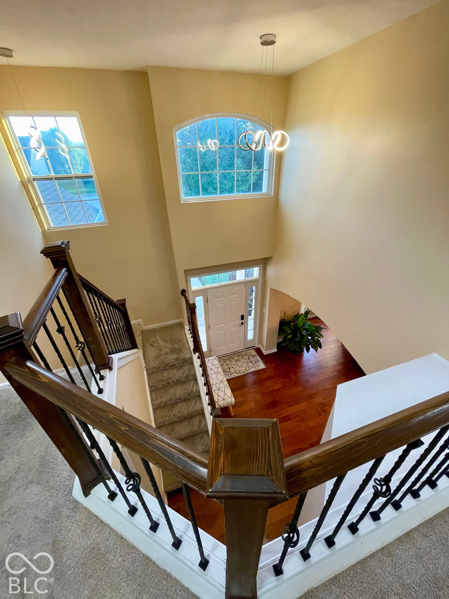 Two-story entry foyer with wood-finish flooring, staircase featuring wrought iron balusters, arched window, and contemporary pendant lighting