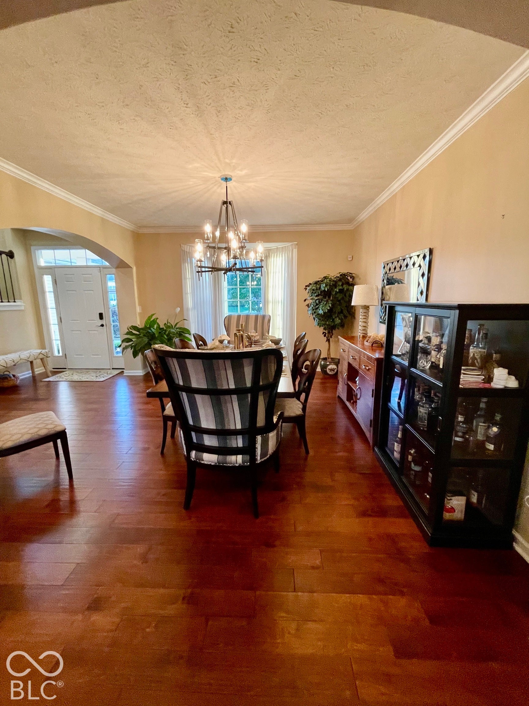 Hardwood flooring throughout, crown molding, arched entry, and a prominent chandelier