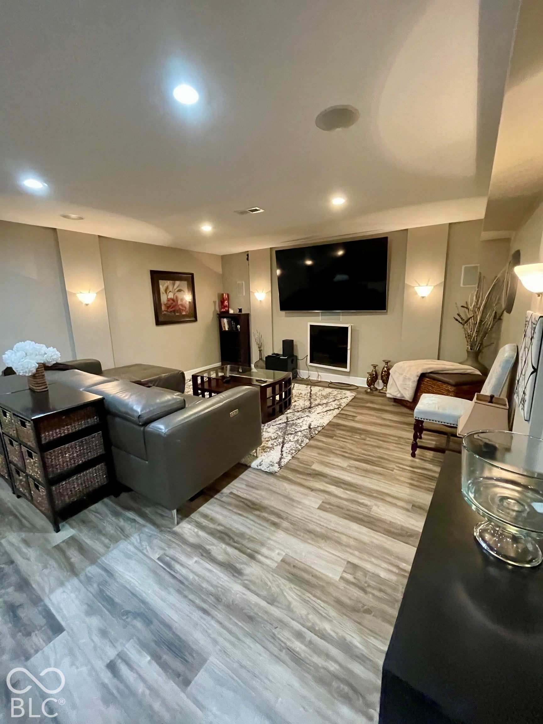Wood-finish flooring, recessed lighting, and wall sconces illuminate this living space