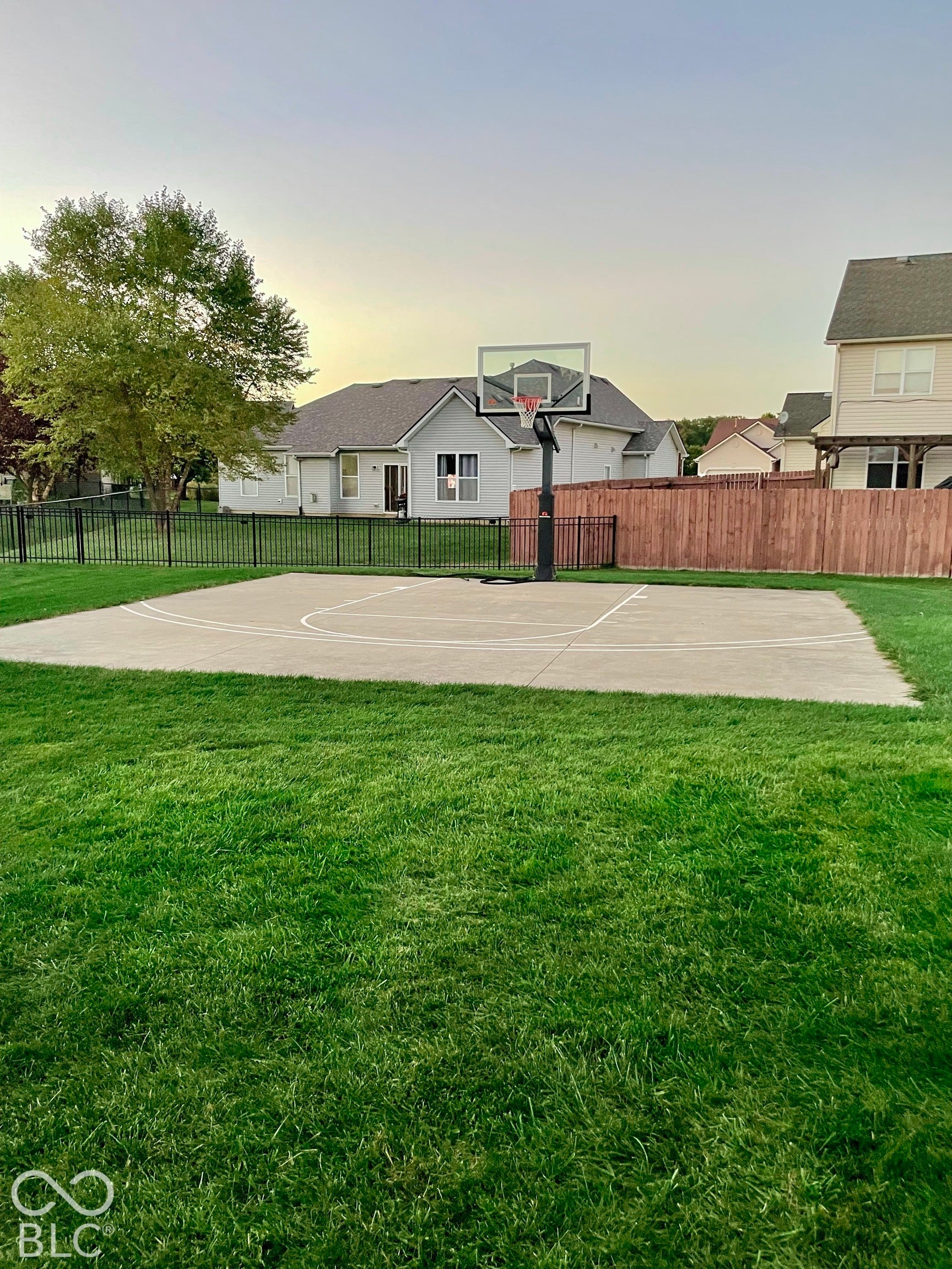 Expansive lawn featuring a concrete sports court with an adjustable basketball hoop