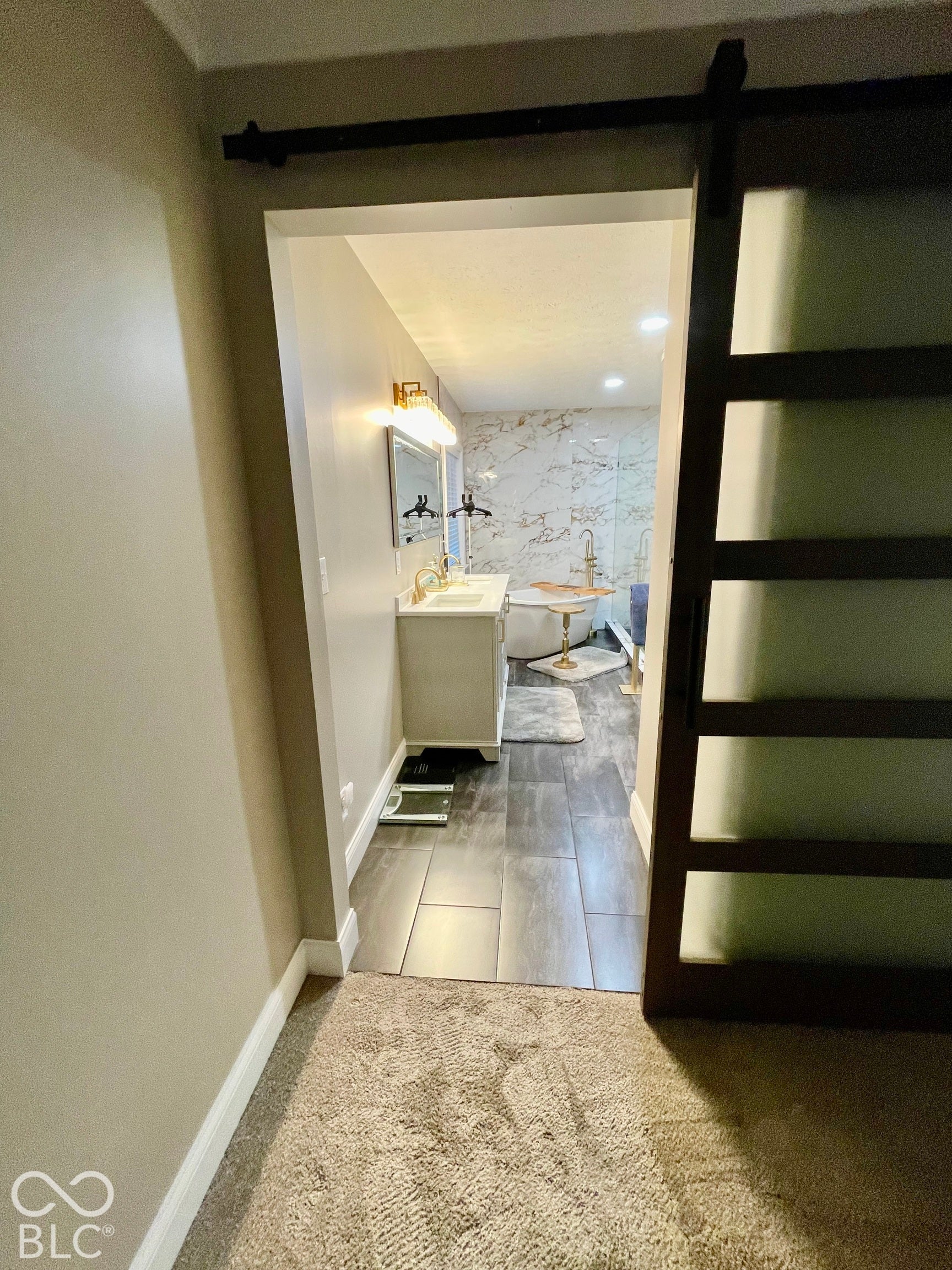 Barn door entry to bathroom with dual vanity, rectangular undermount sinks, and a freestanding bathtub