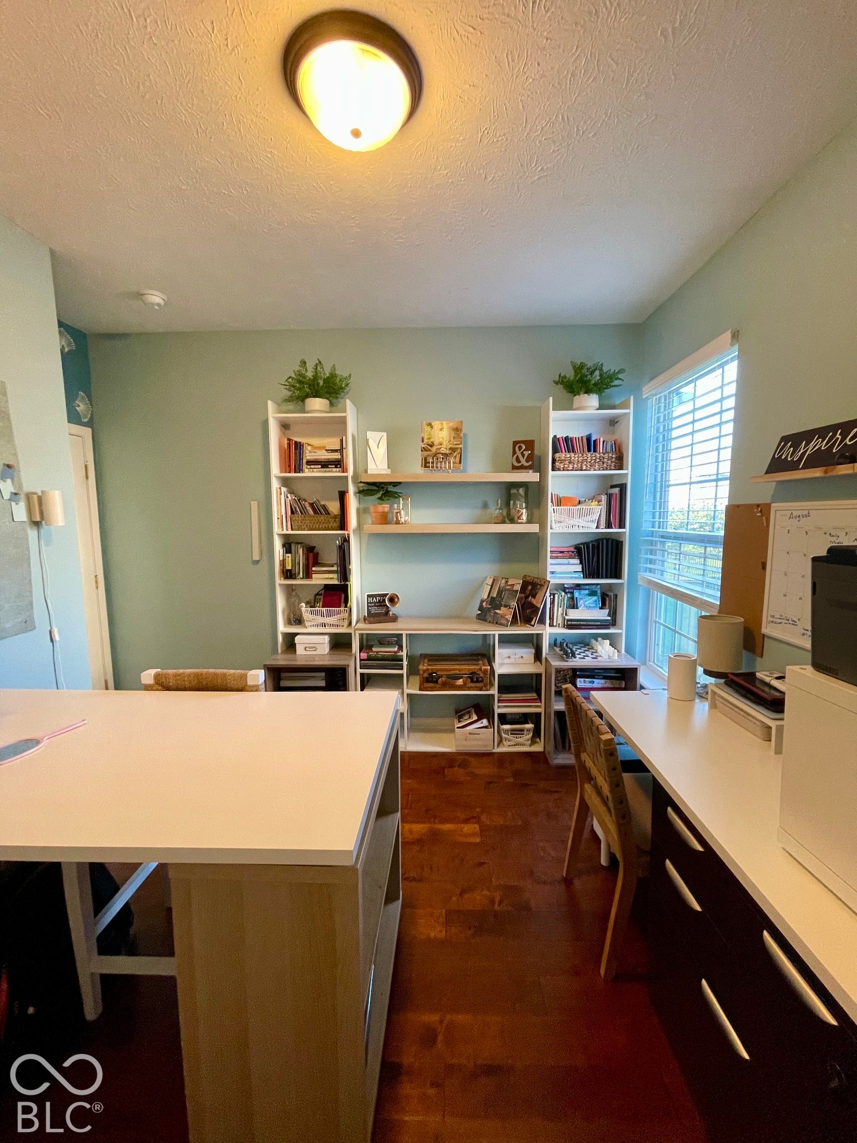 Wood-finish flooring with built-in shelving units, a large window, and a flush mount ceiling light