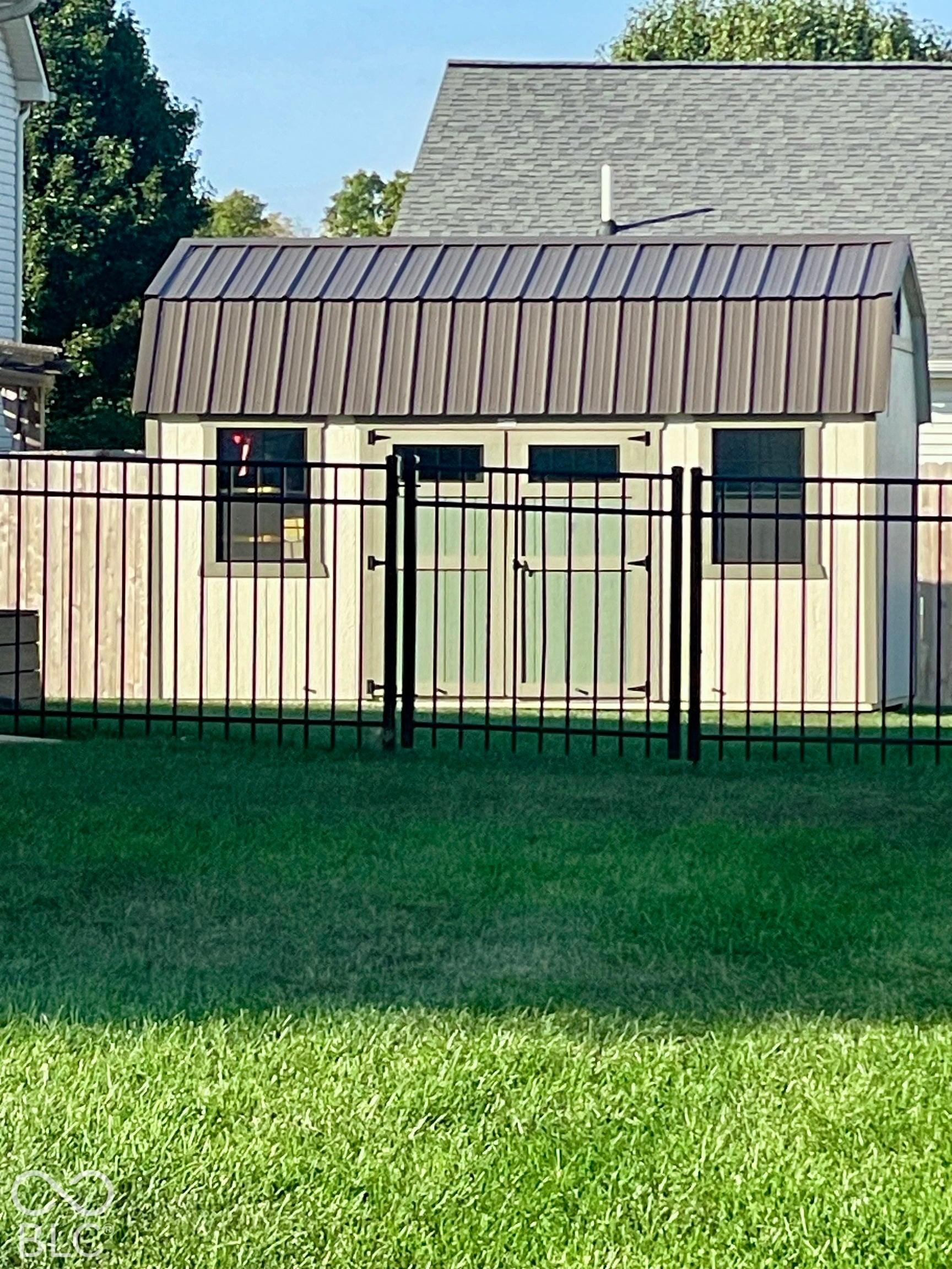 Metal roof shed with double doors, two windows, and a black wrought iron fence