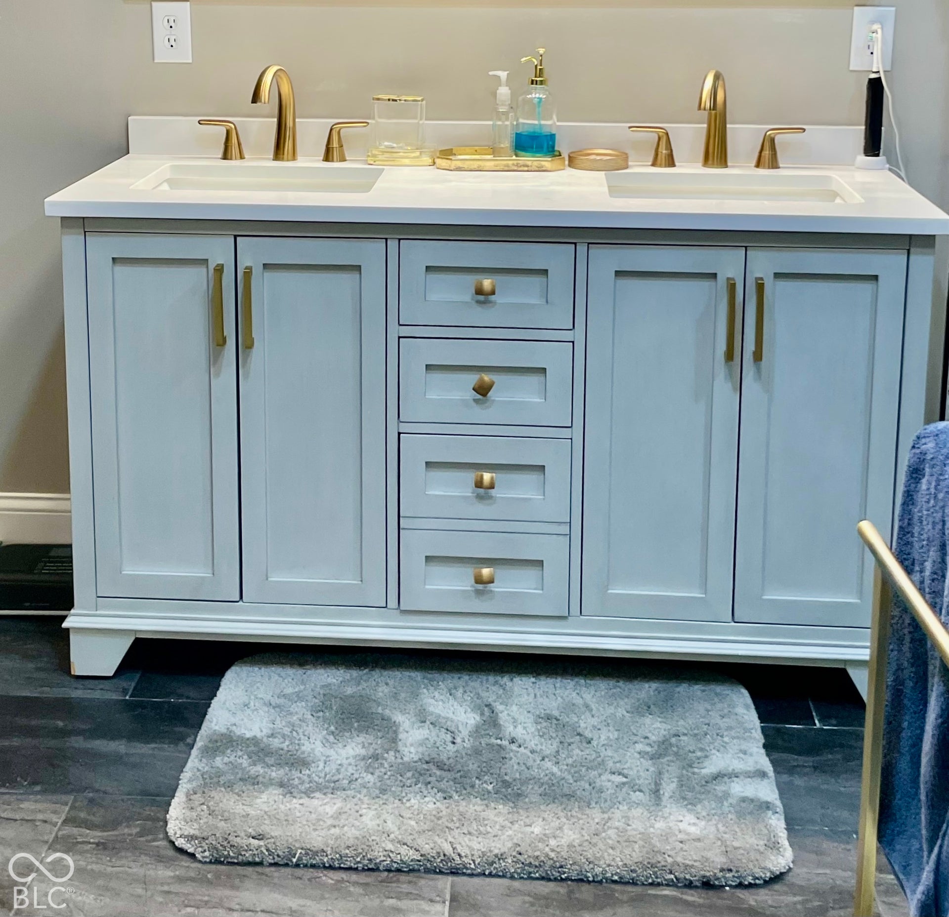 Dual vanity with cabinetry, gold-finish hardware, integrated sinks, and a light-toned countertop