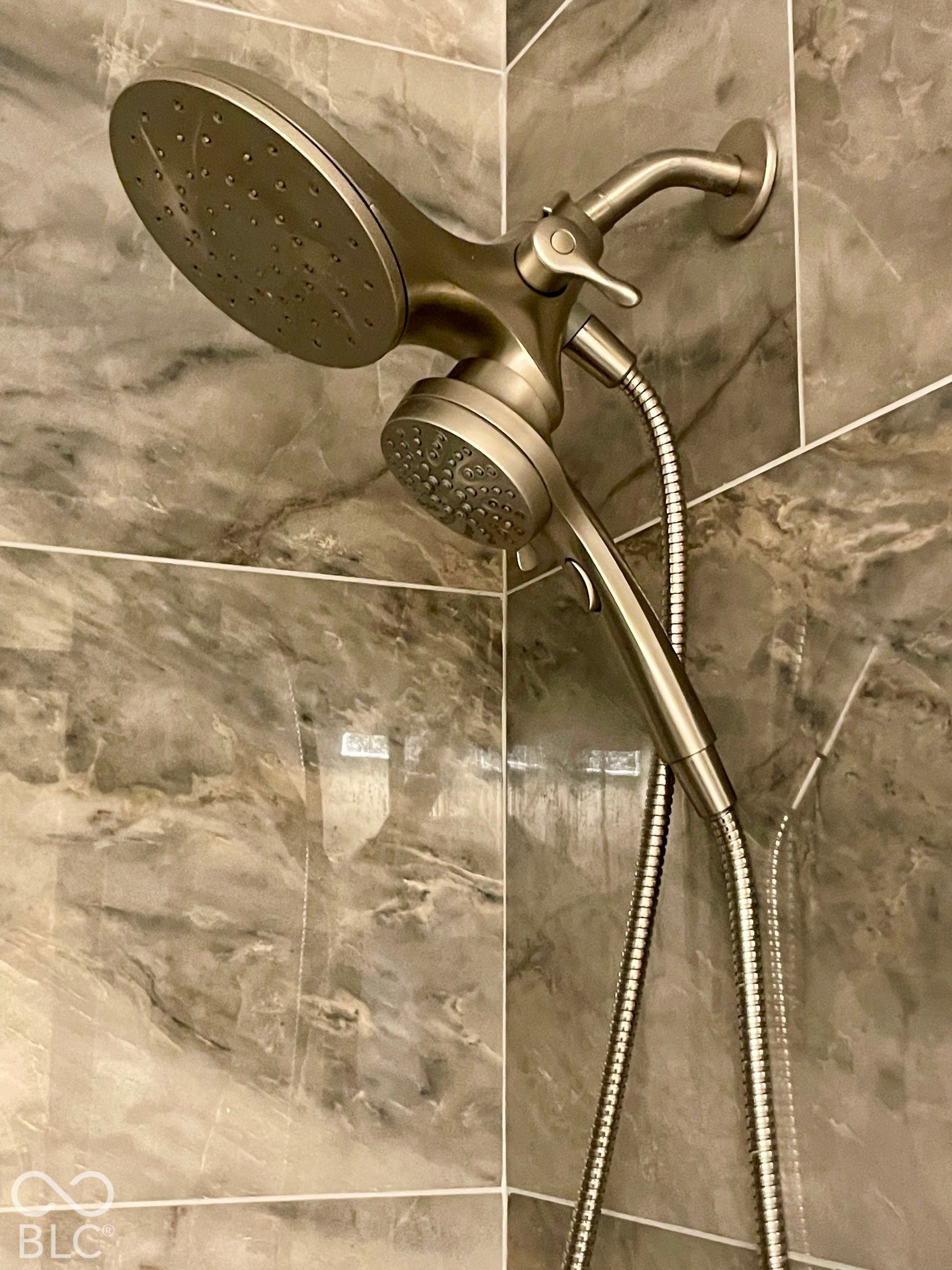 Dual shower head system with a handheld sprayer, set against large format wall tiles...Hall Bath