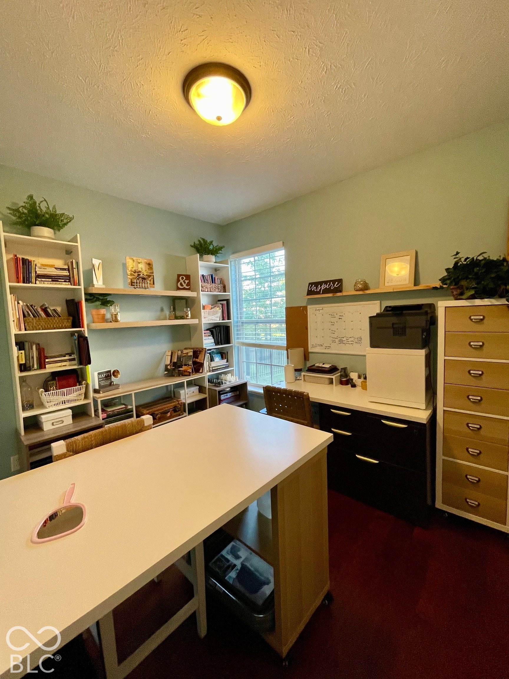 Window with natural light, a ceiling-mounted light fixture, built-in shelving, a wood-finish desk, and dark flooring