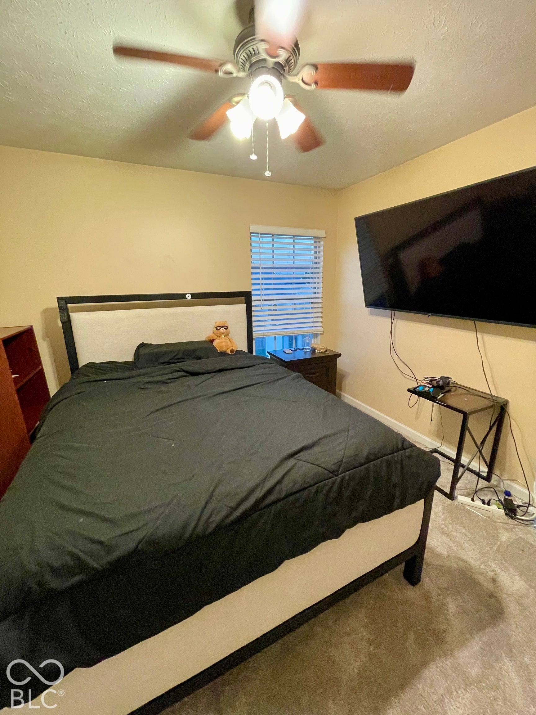 Textured carpeting, window with horizontal blinds, ceiling fan with integrated lighting, and wall-mounted television...Bedroom #2