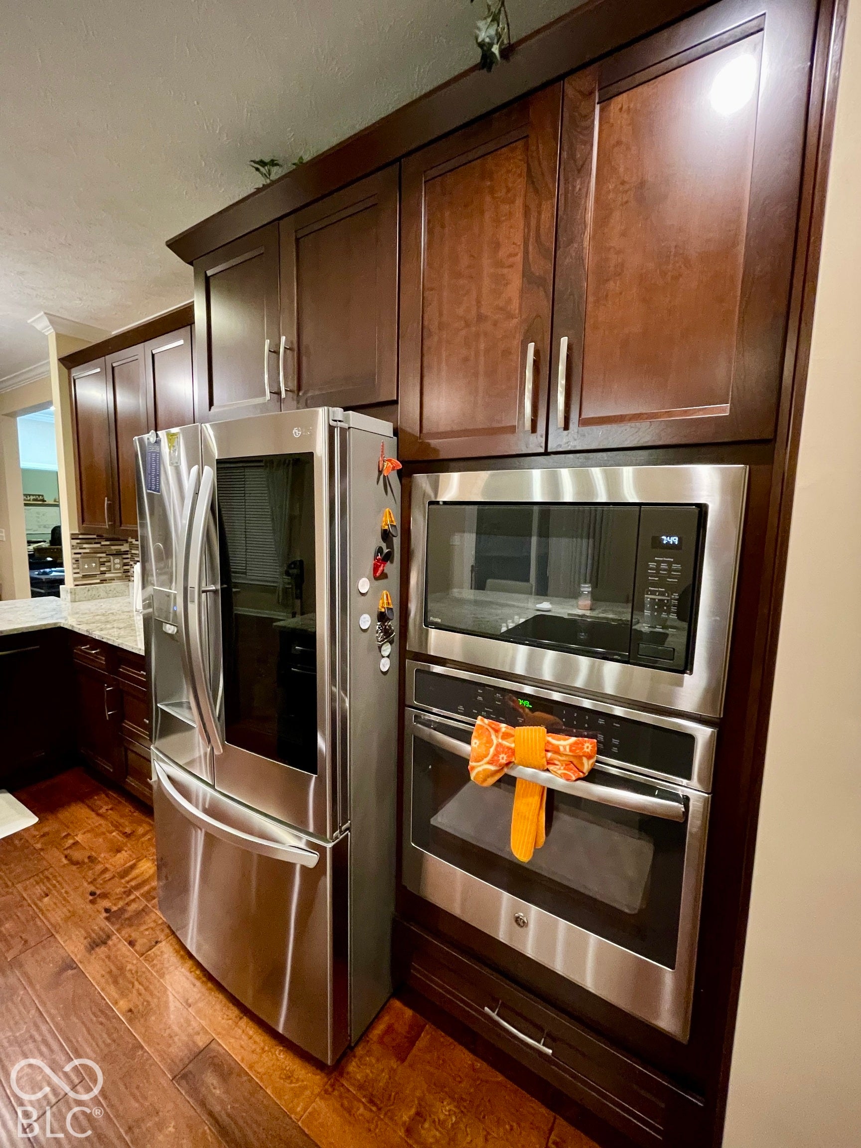 Rich wood-finish cabinetry with crown molding, stainless steel appliances, wood-finish flooring, and a stone-finish countertop