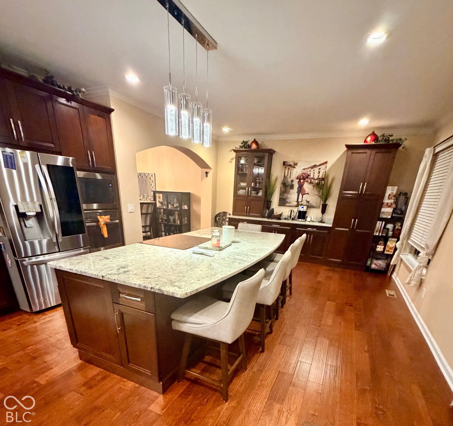 Gourmet kitchen with wood-finish flooring, a large island with a light-toned countertop, dark wood cabinetry, and stainless steel appliances