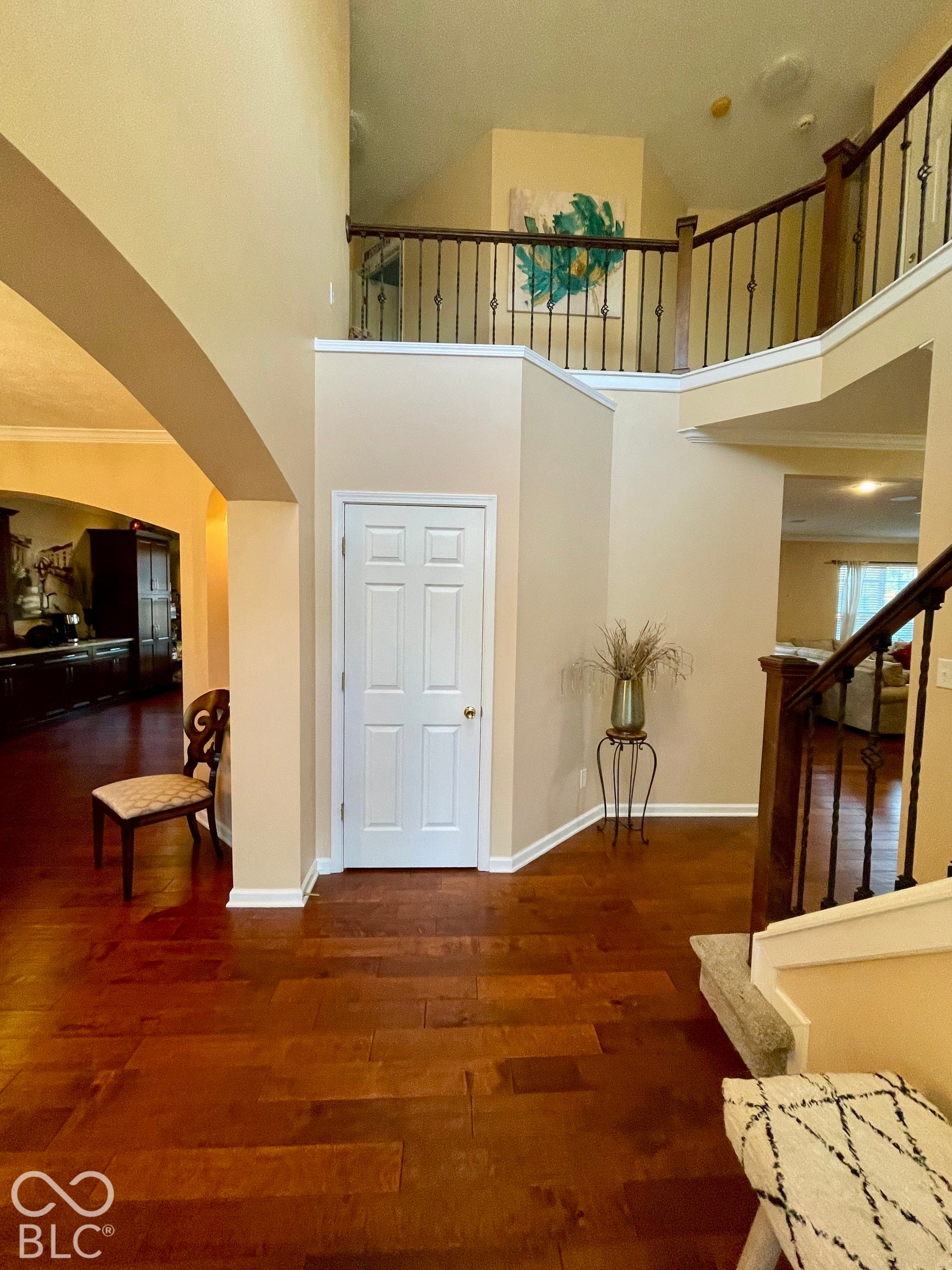Two-story foyer with rich wood-finish flooring and beautiful staircase featuring dark wood and wrought iron balusters