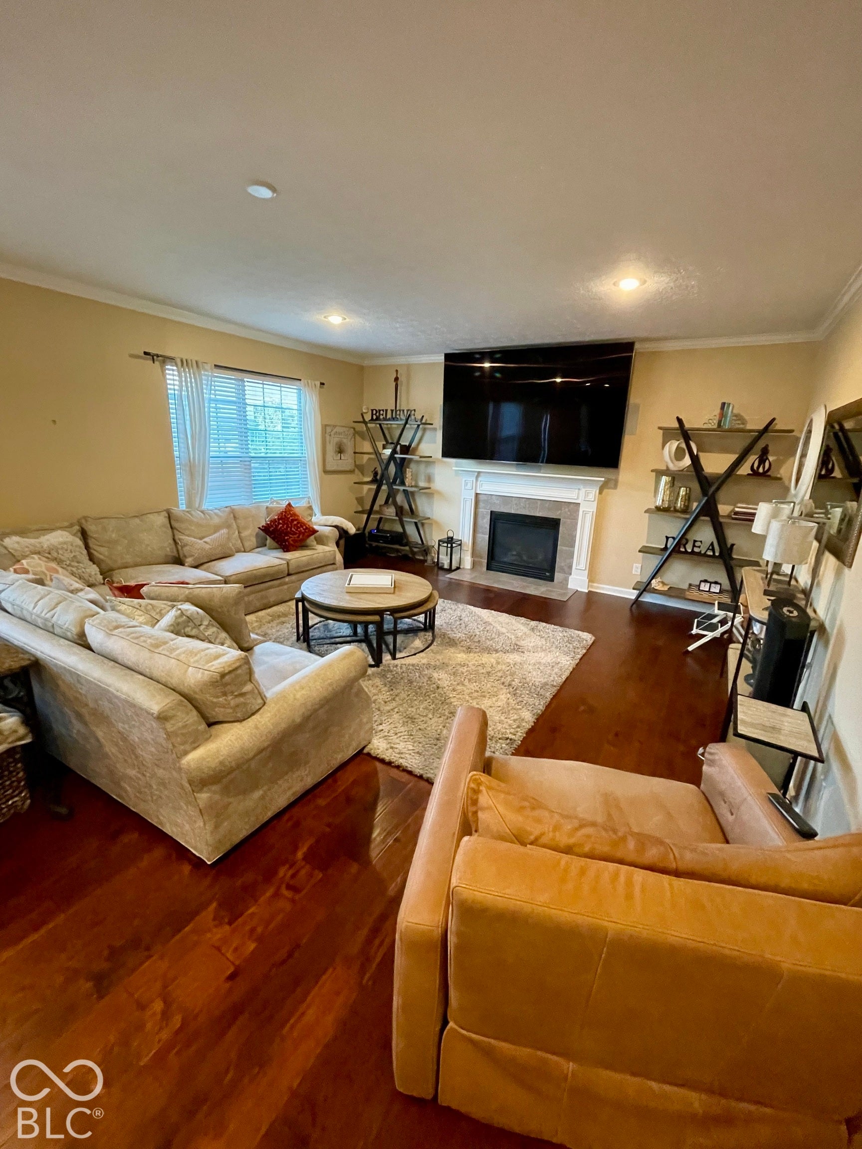 Wood-finish flooring throughout, crown molding, recessed lighting, and a fireplace with a tile surround and mantel