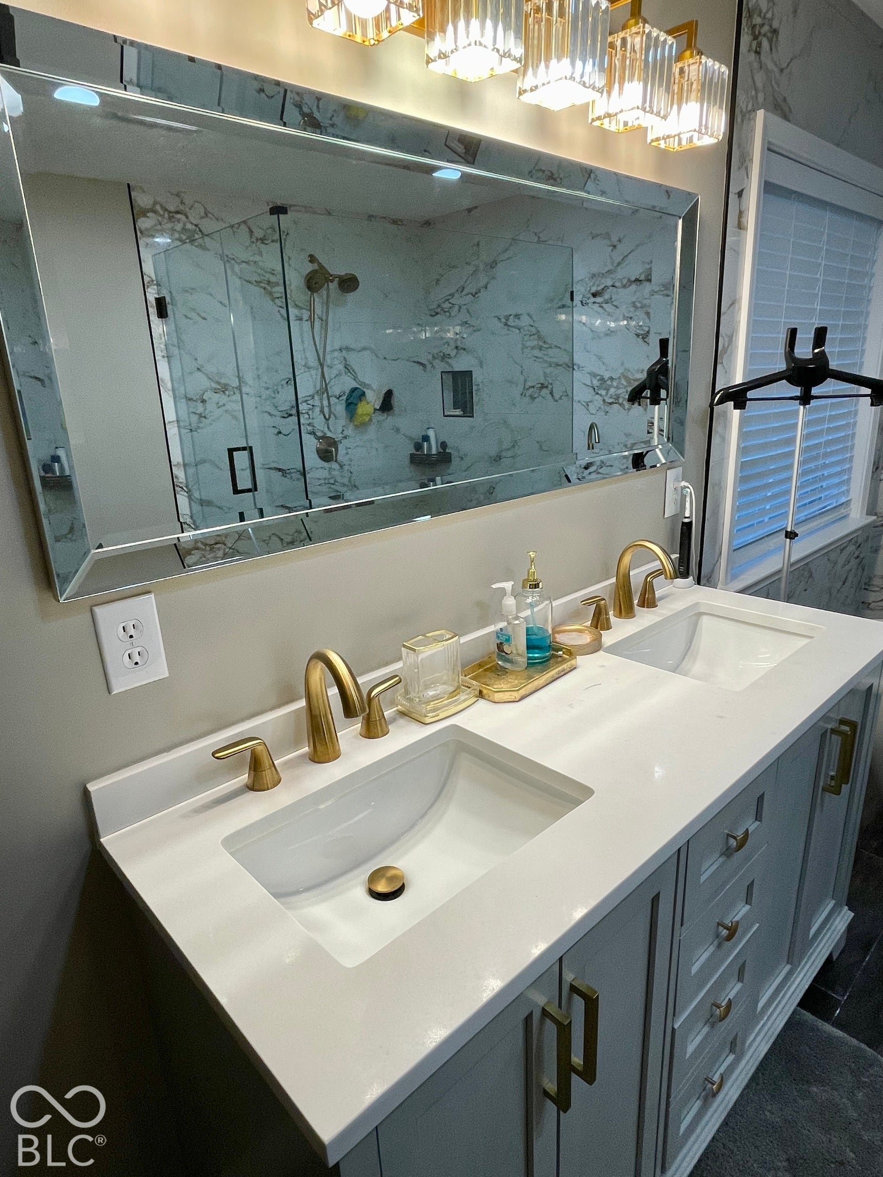 Dual undermount sinks with brushed gold fixtures, white countertop, vanity with gold hardware, and a framed mirror