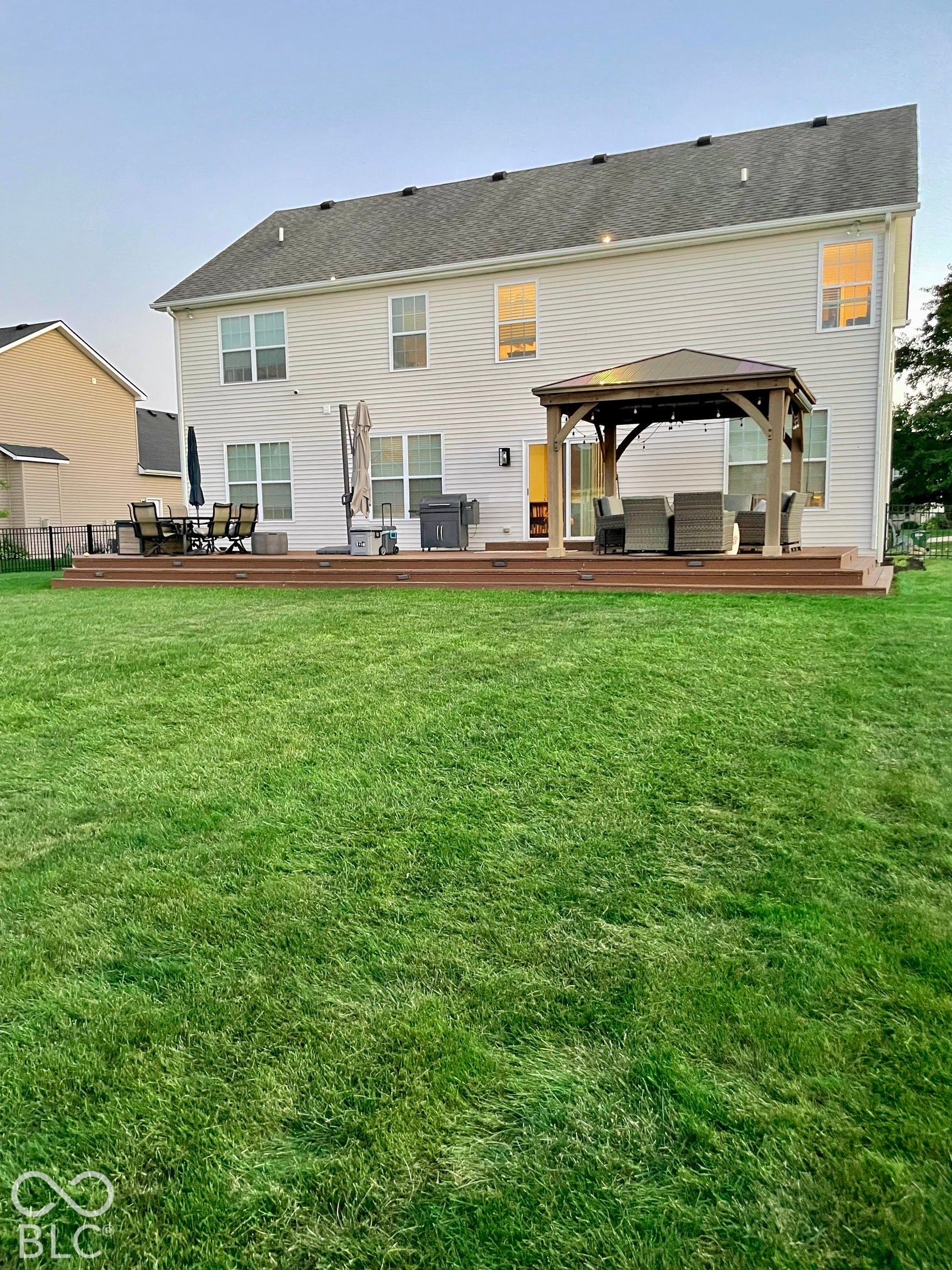Expansive green lawn with a multi-level composite deck, featuring a built-in gazebo and sliding glass door access to the residence