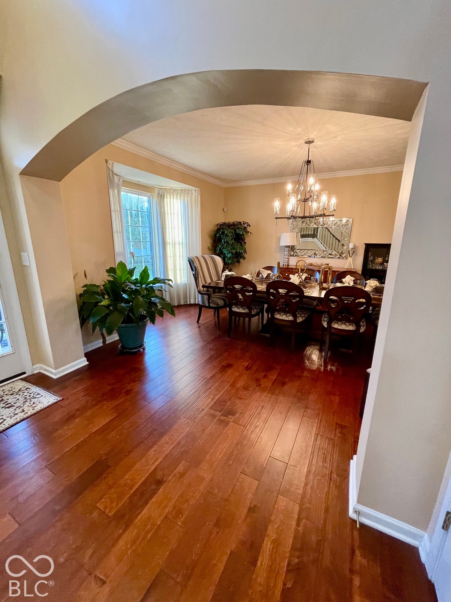 Hardwood flooring throughout, arched doorway, bay window, chandelier lighting fixture, and crown molding