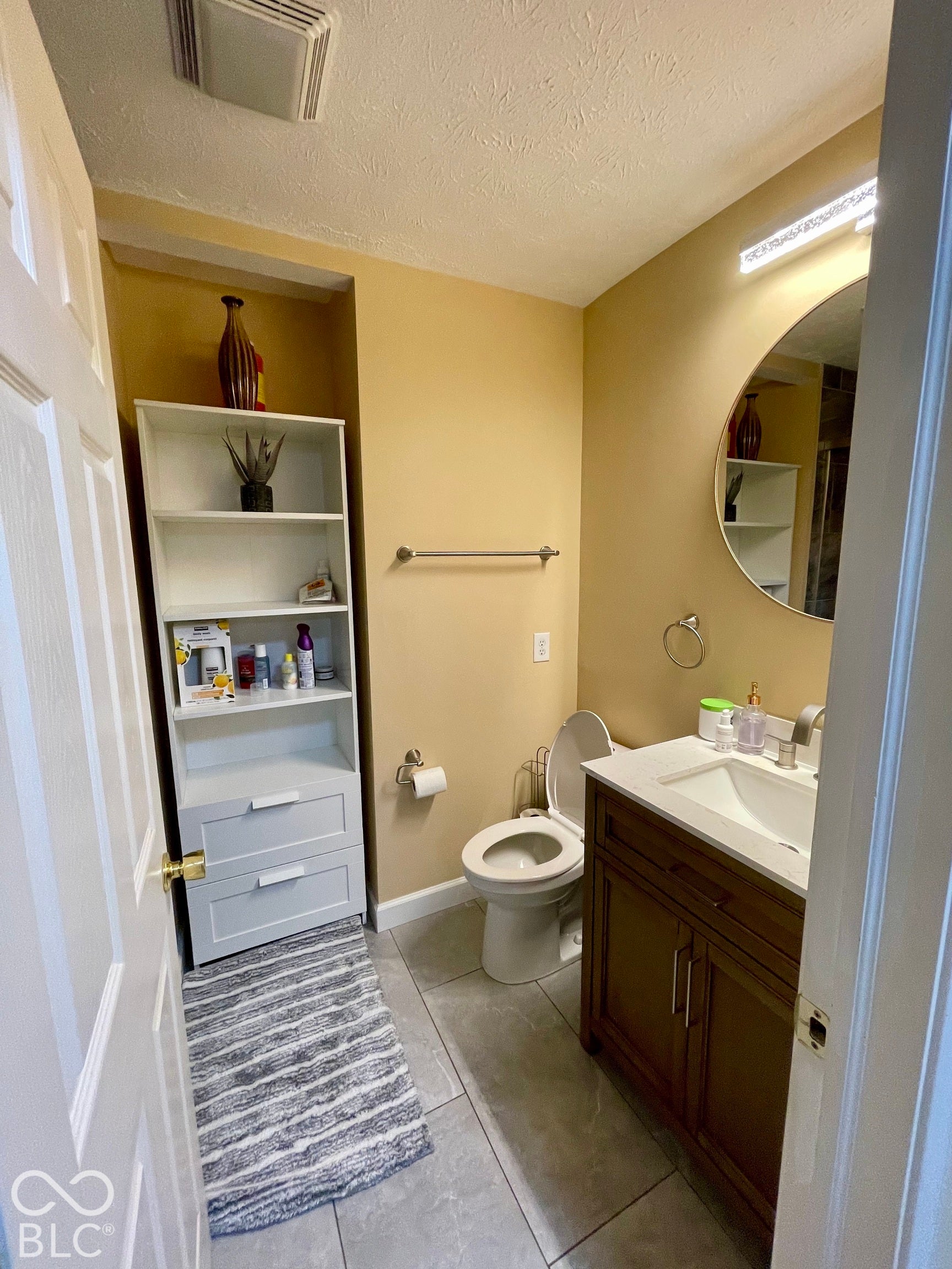 Vanity with a white countertop and undermount sink, round mirror, and tile flooring...Hall Bath