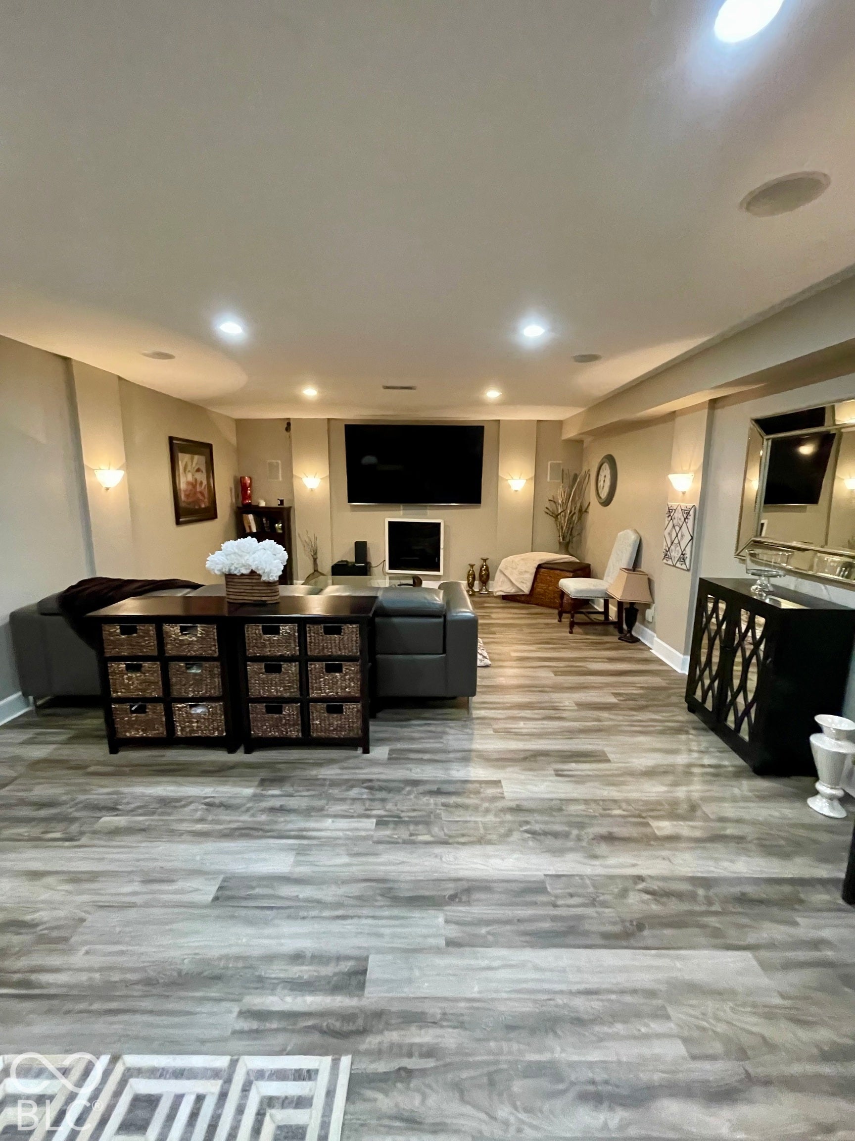 Recessed lighting throughout, wood-finish flooring, built-in ceiling speakers, wall-mounted sconce lighting, and a fireplace with a white mantel