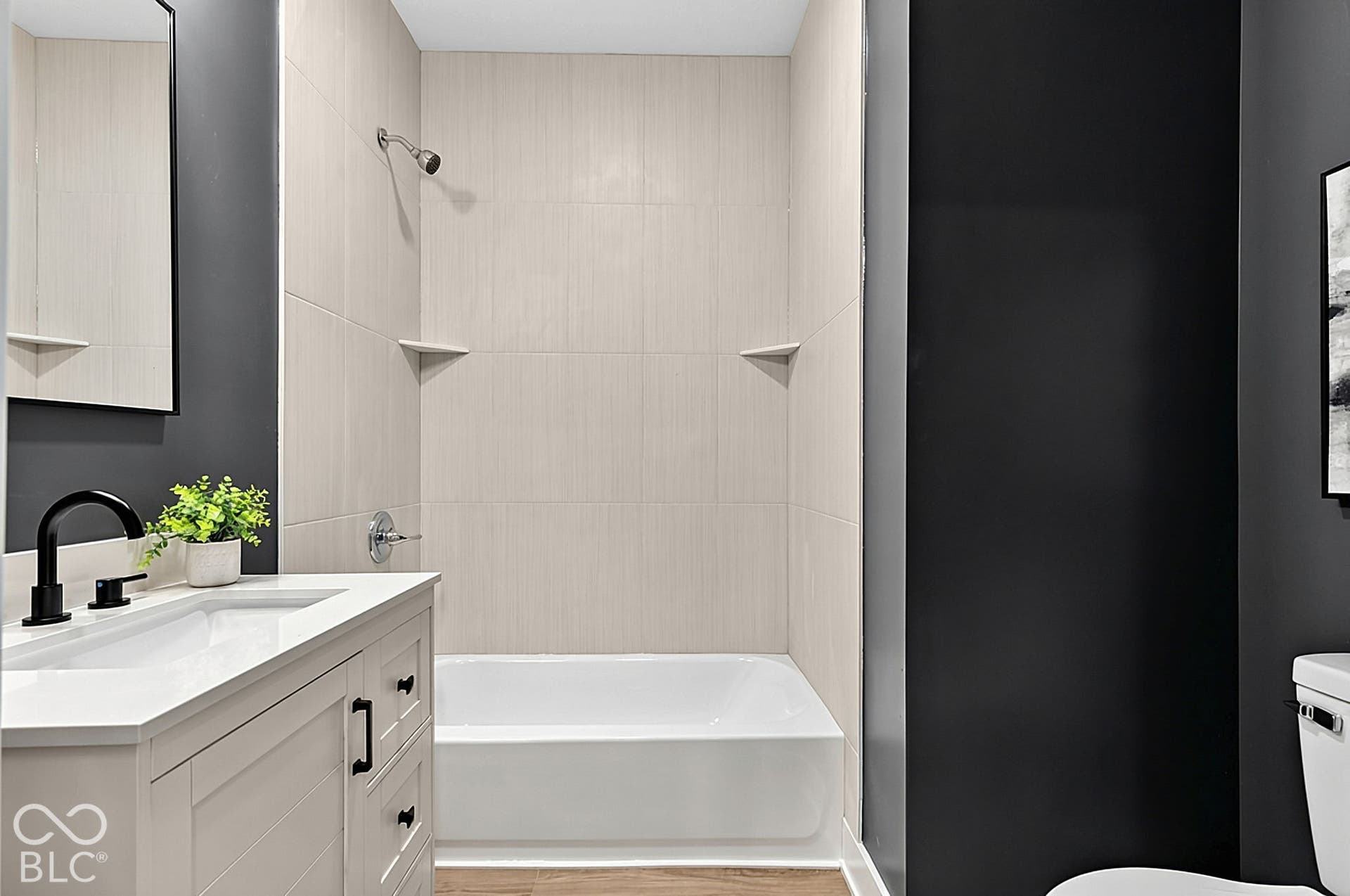 Bathroom featuring a white vanity with a composite countertop, undermount sink, matte black faucet, and a tiled shower-tub surround with built-in corner shelving