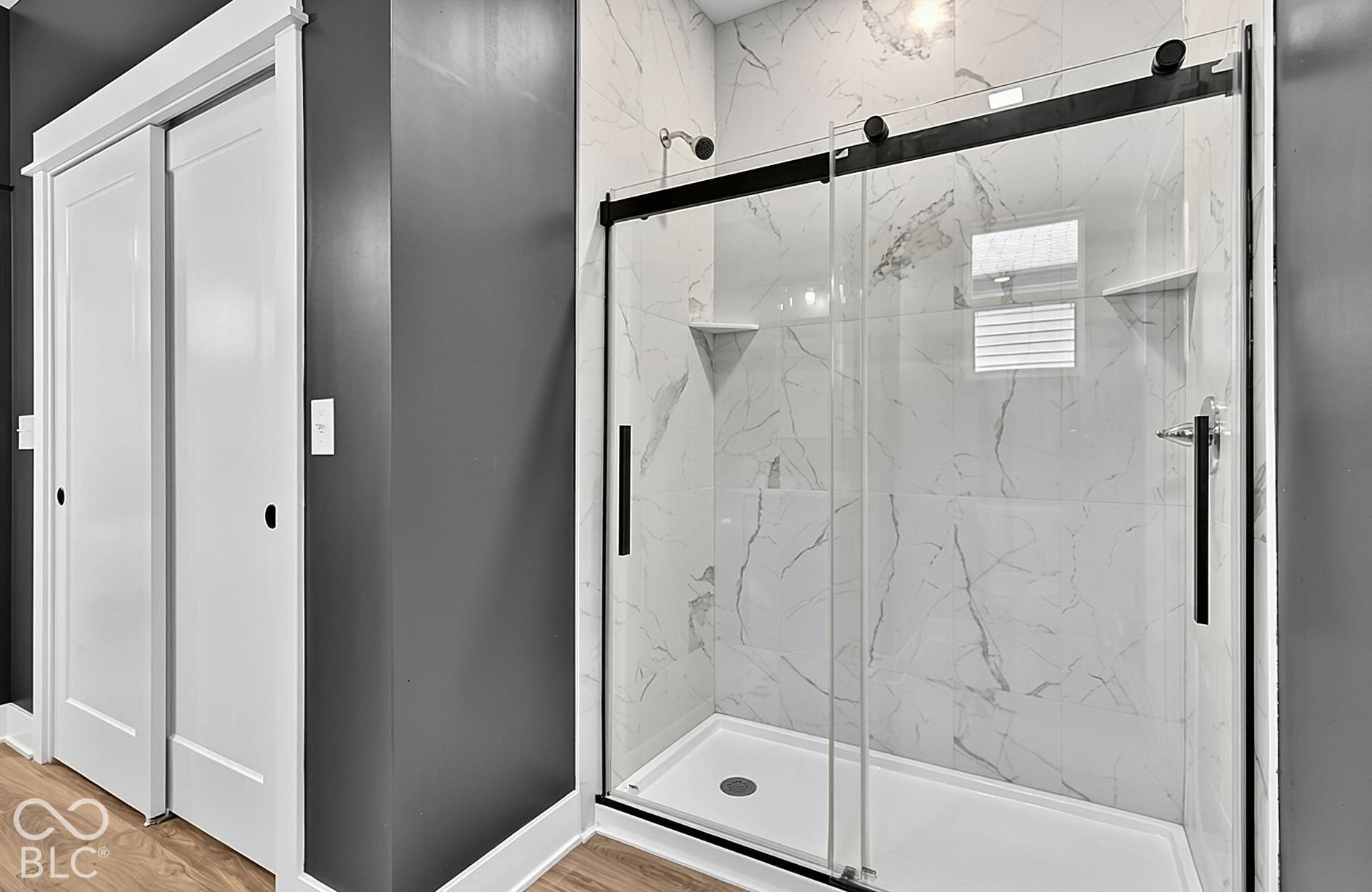 Walk-in shower featuring floor-to-ceiling stone-pattern tile, a glass sliding door with matte black hardware, built-in shelving, and white sliding closet doors