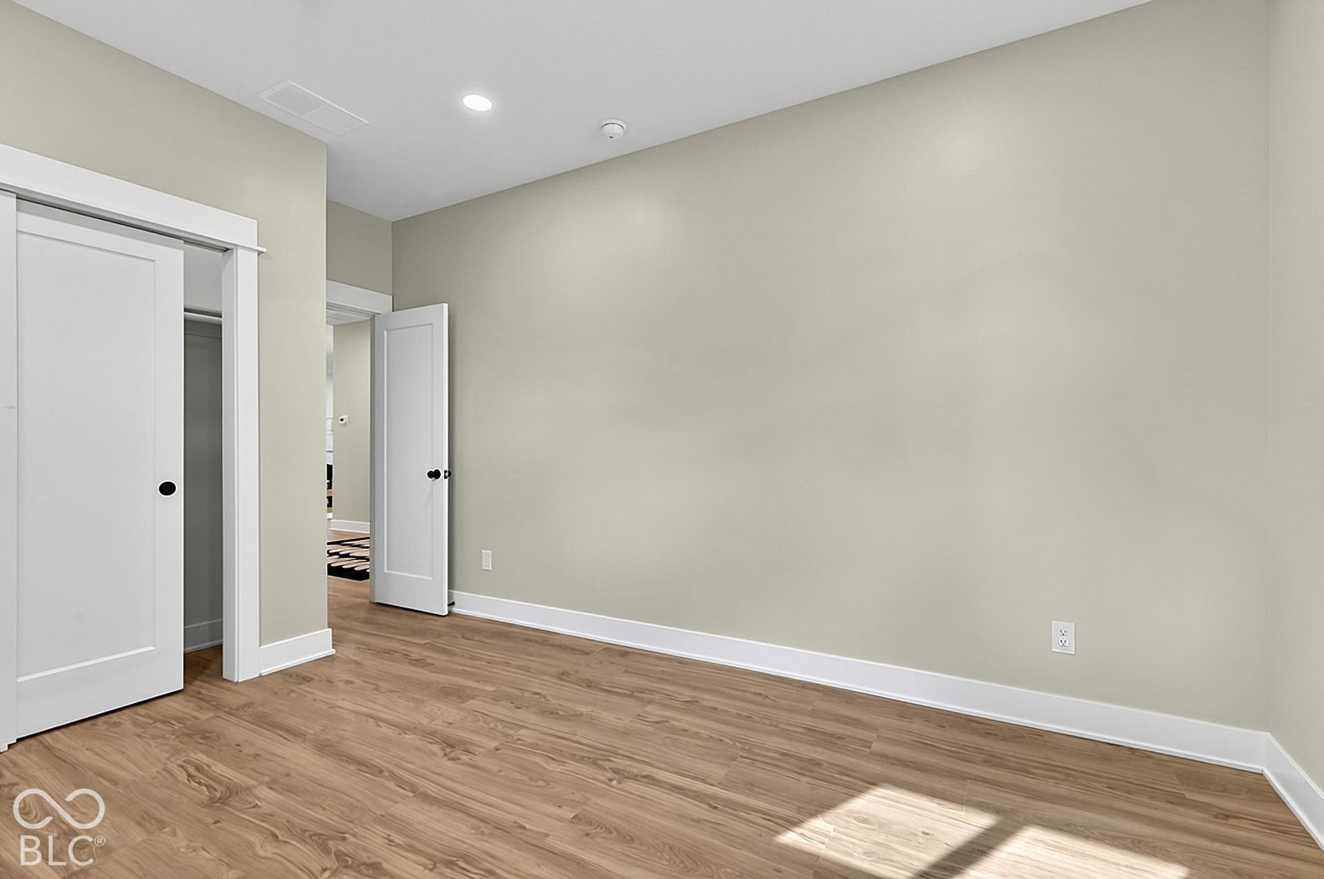 Neutral-toned interior space featuring wood-finish flooring, white shaker-style interior doors, recessed lighting, and crisp white door casings