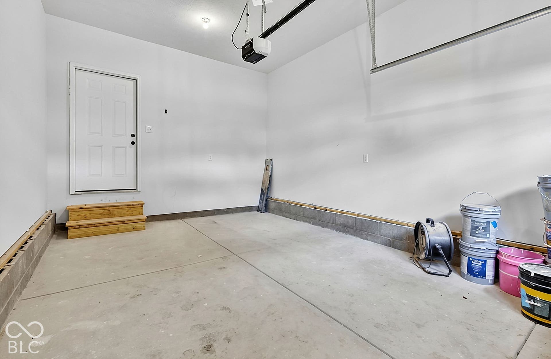 Attached two-car garage featuring a concrete floor, finished white walls, and a dedicated service door with wooden steps