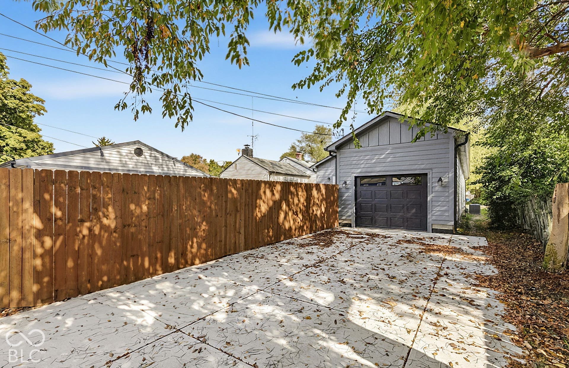 Detached garage featuring grey siding, a sectional door, and exterior wall-mounted light fixtures, complemented by a concrete parking pad and a wood privacy fence