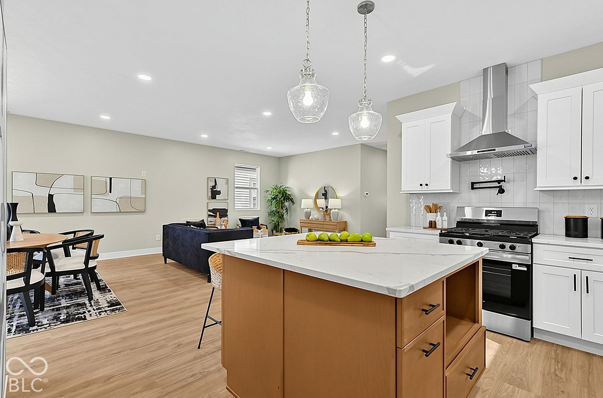 Kitchen featuring a center island with light-toned surfacing, white cabinetry, stainless steel range with overhead chimney hood, wood-finish flooring, and glass pendant lighting