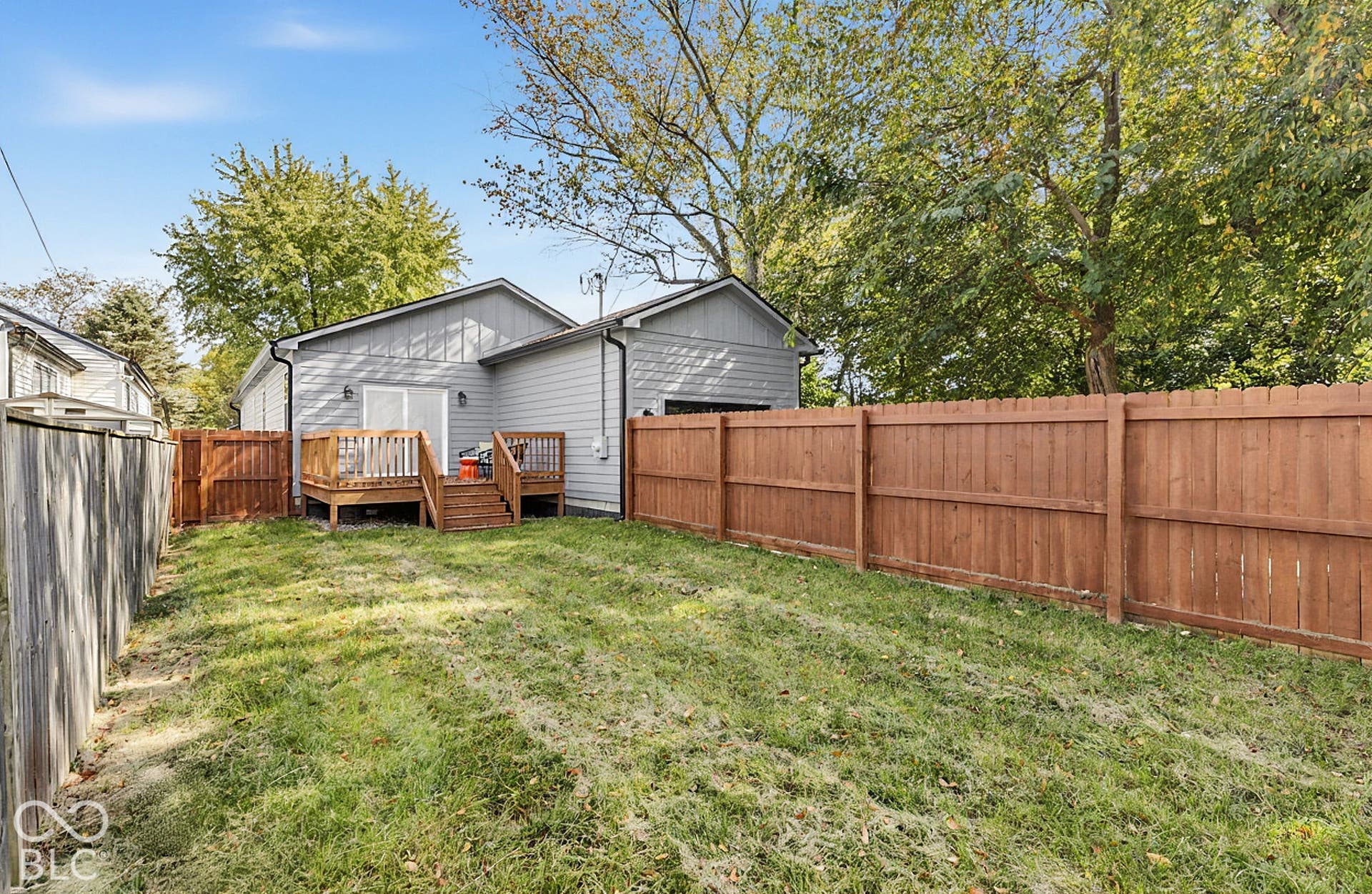 Rear exterior featuring horizontal lap siding, an elevated wood deck, and a full-height wood privacy fence enclosing the backyard