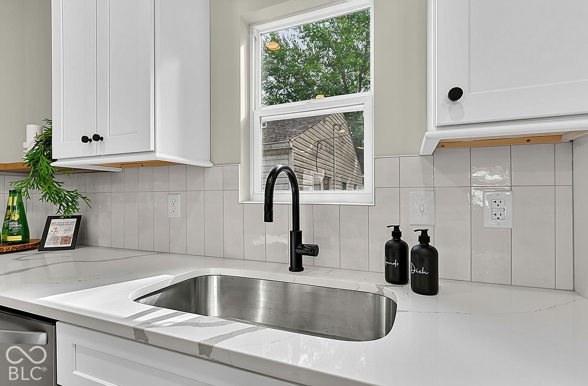 White Shaker-style cabinetry, white countertops with grey veining, vertical subway tile backsplash, stainless steel undermount sink, and matte black gooseneck faucet