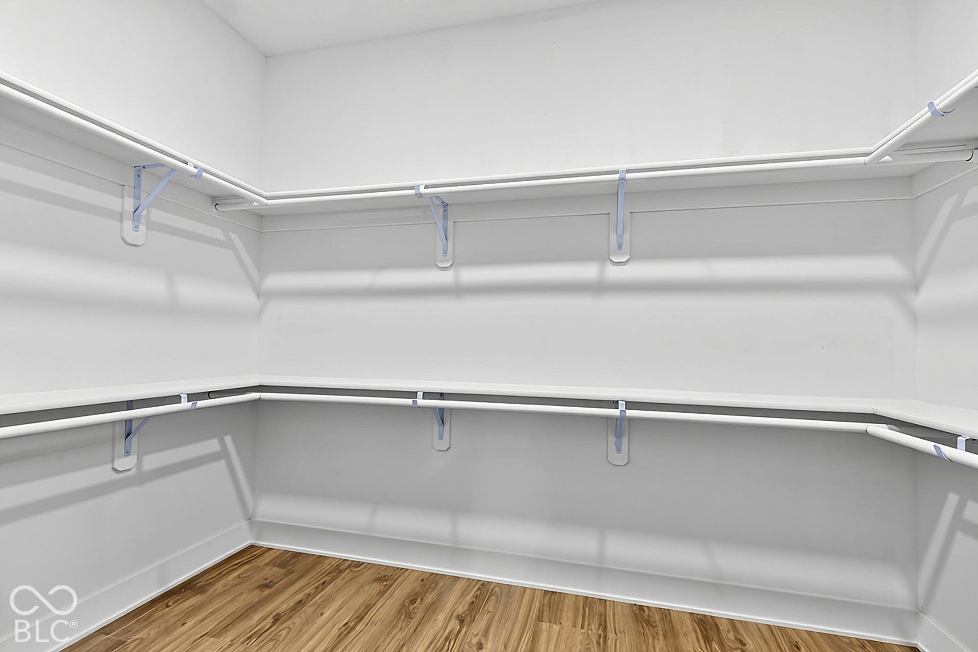 Walk-in closet featuring wood-finish flooring and dual tiers of white wire shelving with integrated hanging rods