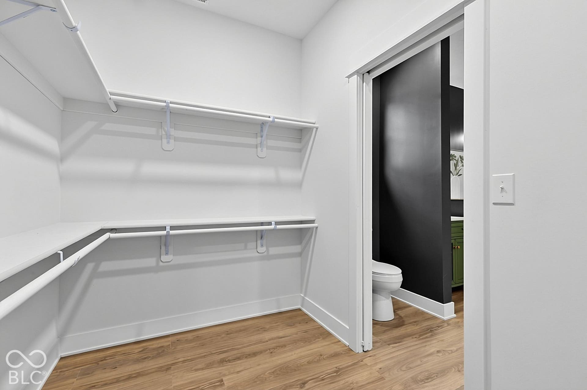 Walk-in closet featuring multi-level built-in shelving, wood-finish flooring, and a sliding door