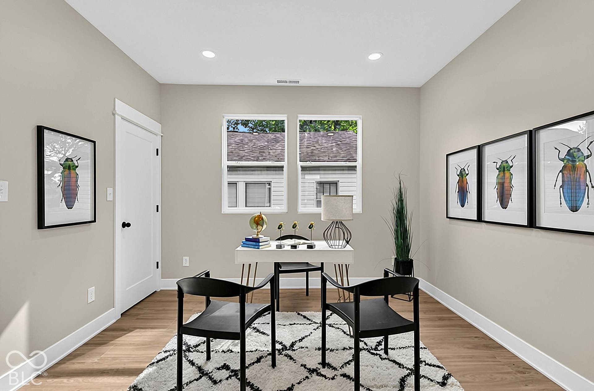 Neutral-toned interior room featuring wood-finish flooring, dual windows with white casings, recessed lighting, and a crisp, white-paneled door