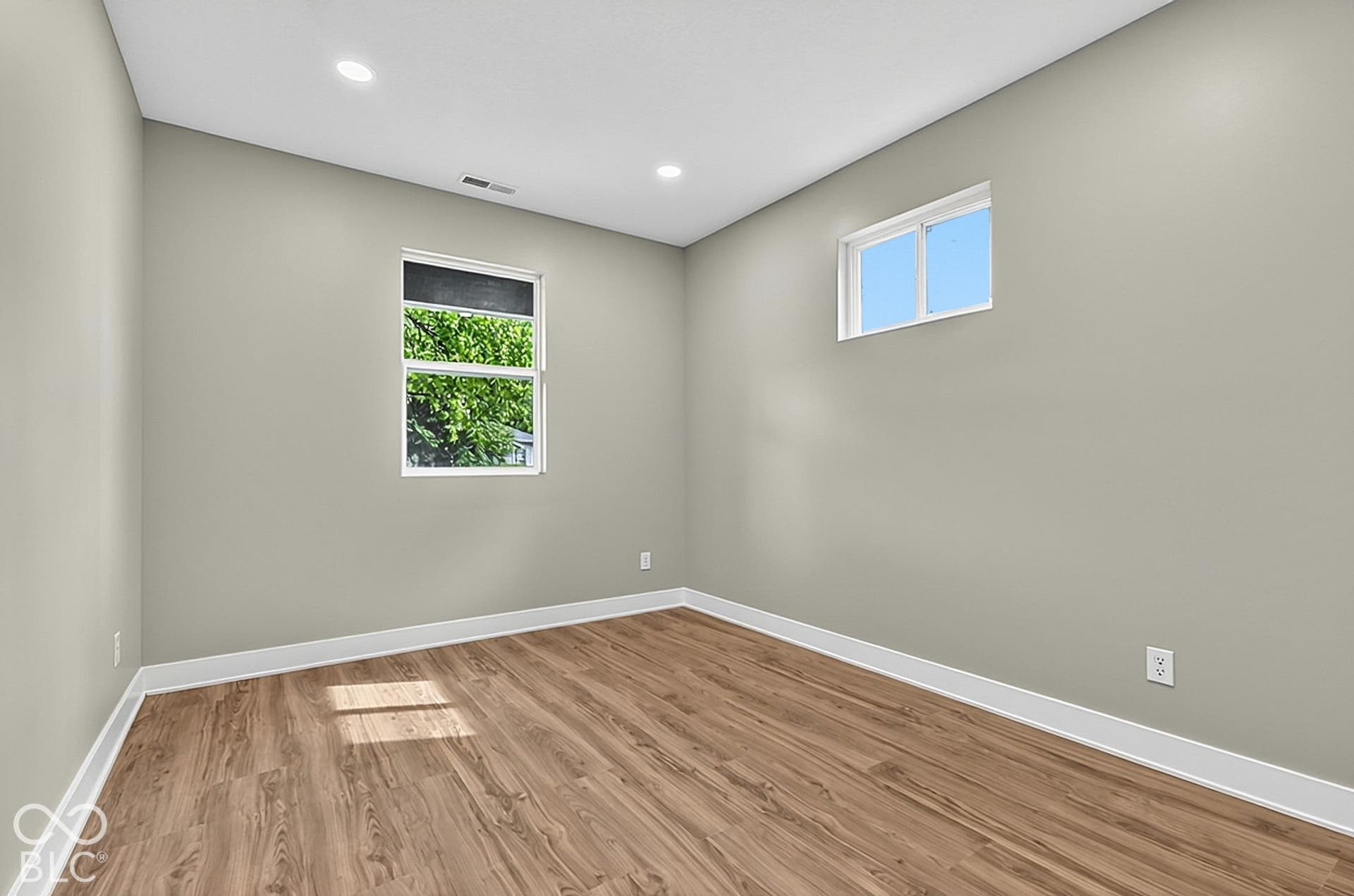 Neutral-toned interior space featuring wood-finish flooring, recessed lighting, and two multi-pane windows