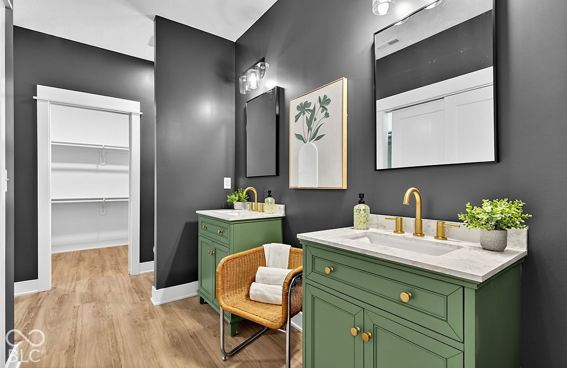 Dual green-toned vanities featuring stone-finish countertops, brass-finish widespread faucets, framed rectangular mirrors, and custom cabinetry, with wood-finish flooring