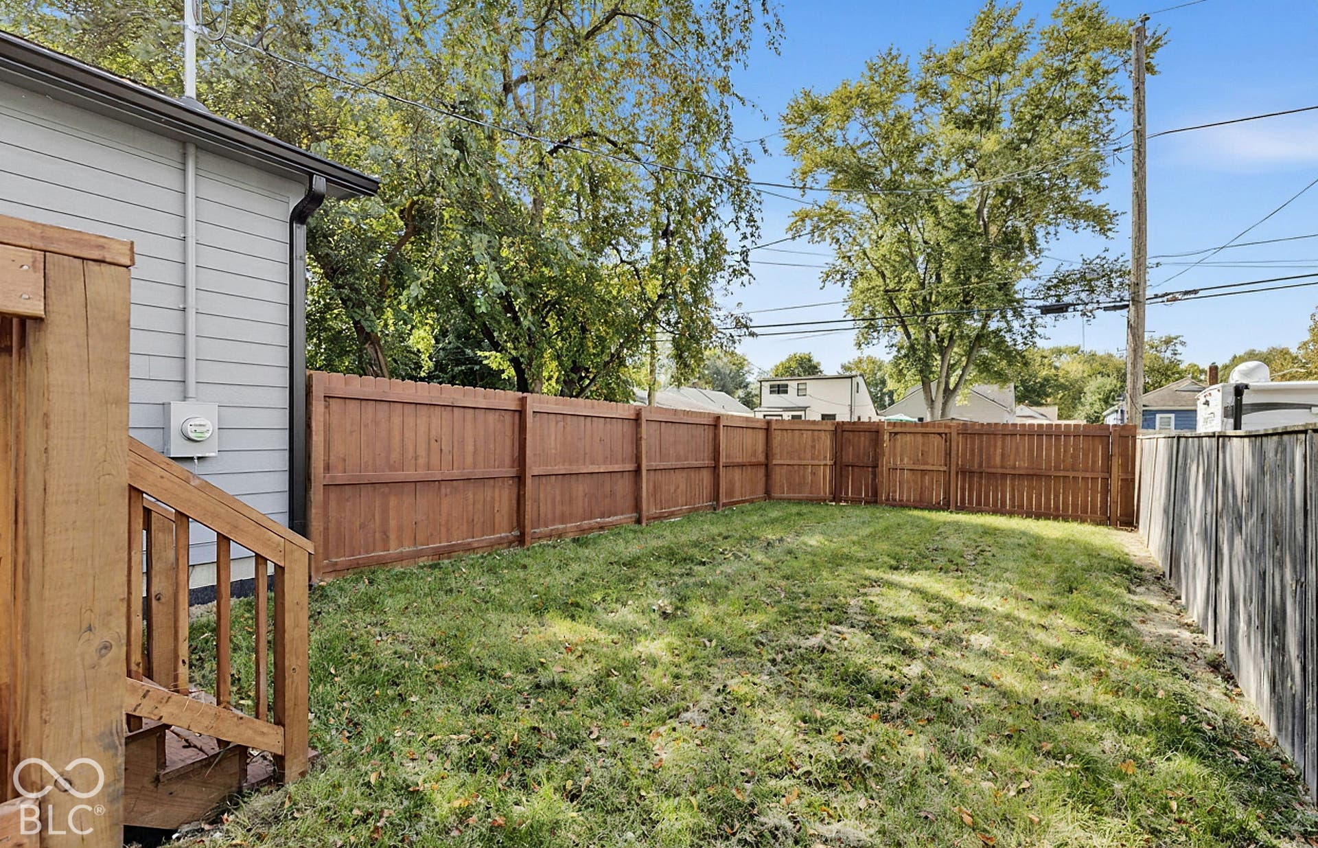 Rear yard featuring a grass lawn, wood-stain privacy fencing, and a wood-finish staircase
