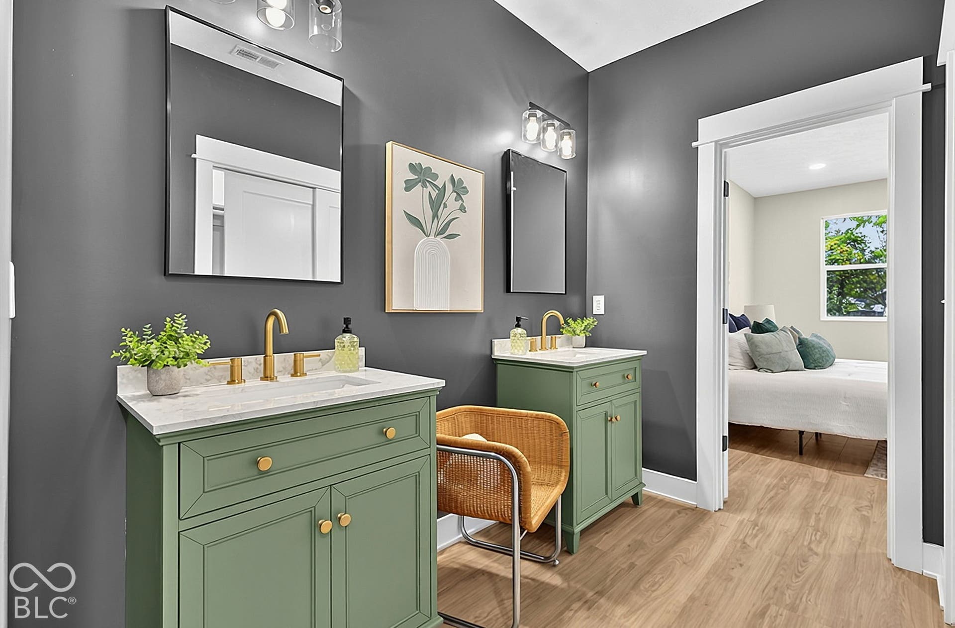 Dual green-painted vanities featuring stone-finish countertops, brass-toned fixtures, rectangular mirrors, and wood-finish flooring
