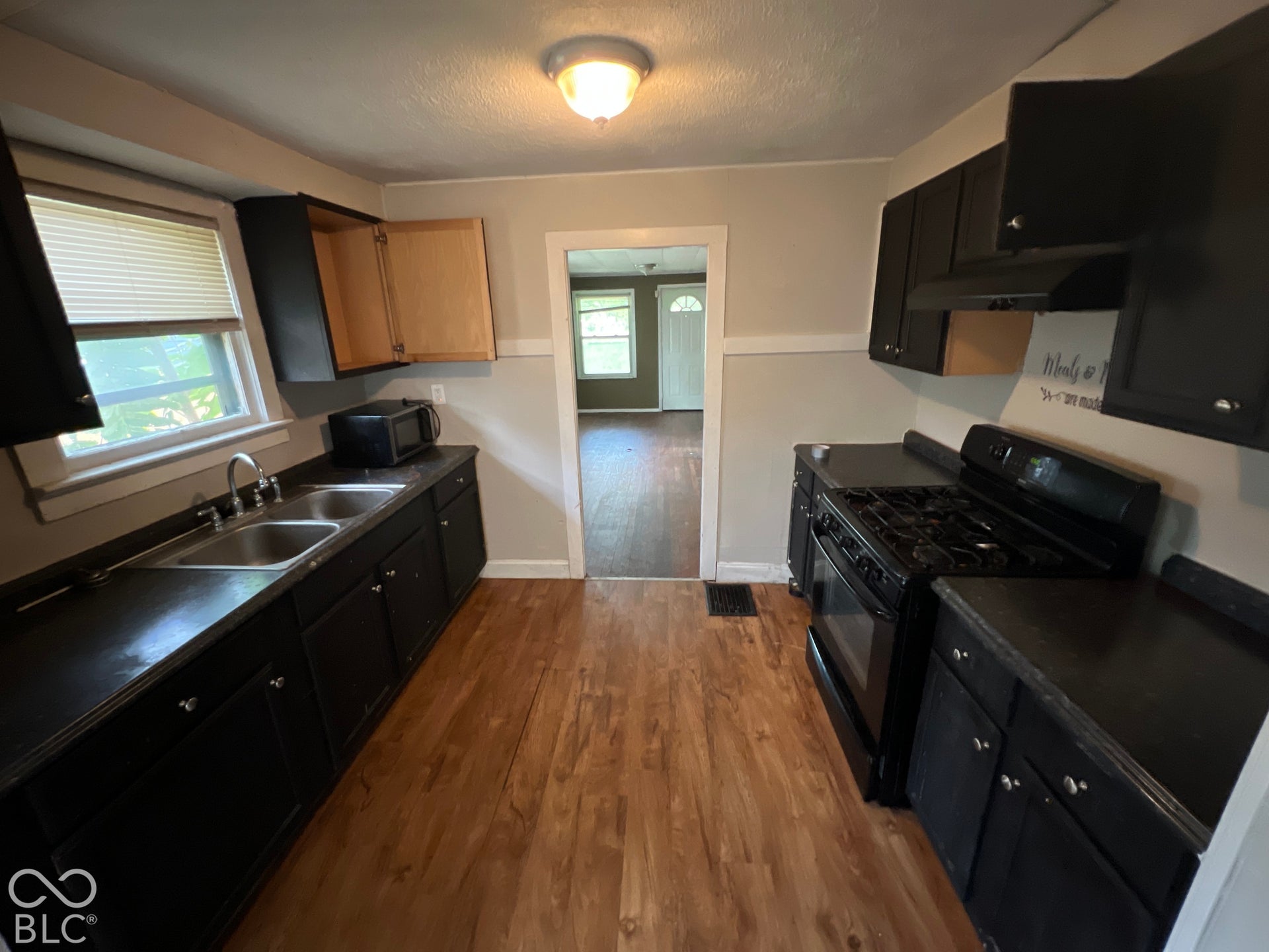 1431 W Pruitt Street, Indianapolis, IN 46208 Kitchen featuring wood-finish flooring, black cabinetry, a dual basin stainless steel sink, and a black gas range