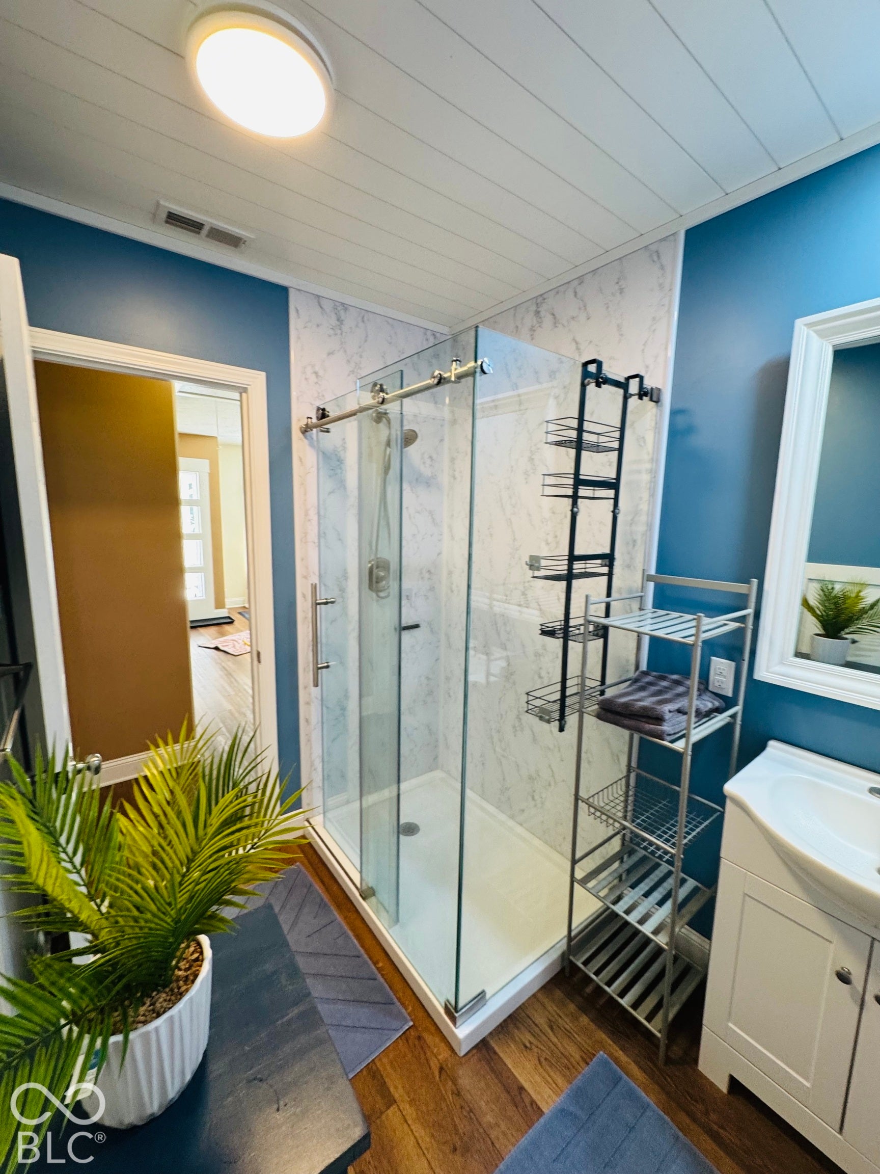 Walk-in shower with sliding glass door, white shiplap ceiling, wood-finish flooring, and a single vanity with storage