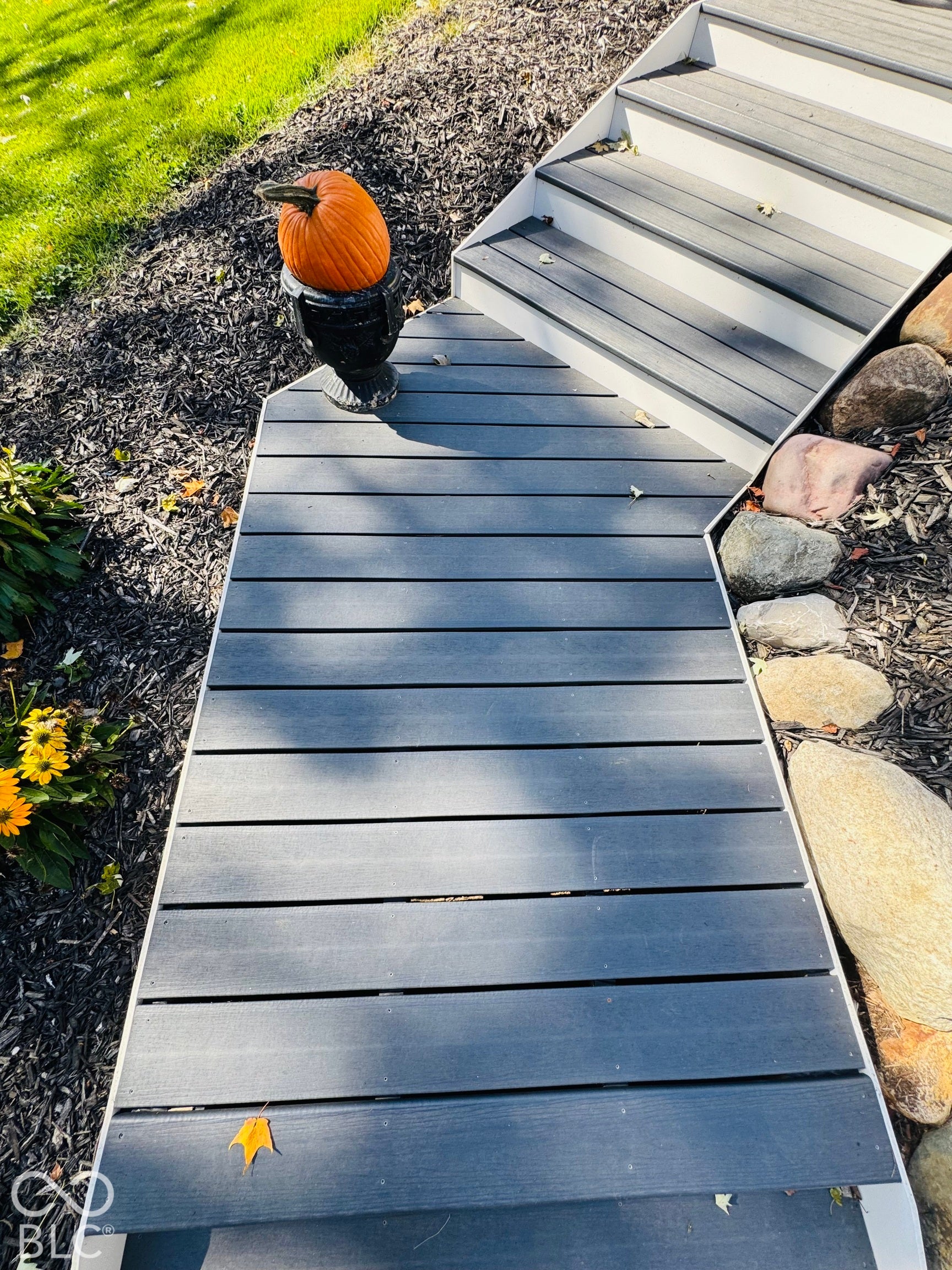 Beautiful Composite front stairs with white risers, bordered by decorative rocks and Beautiful Perennial flowers and custom landscaping