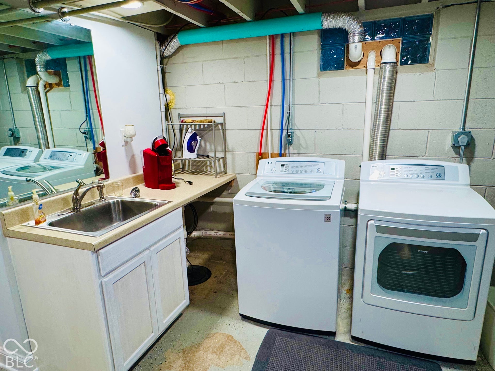 Utility area featuring a stainless steel sink with a chrome faucet, light-toned countertop, and white base cabinetry